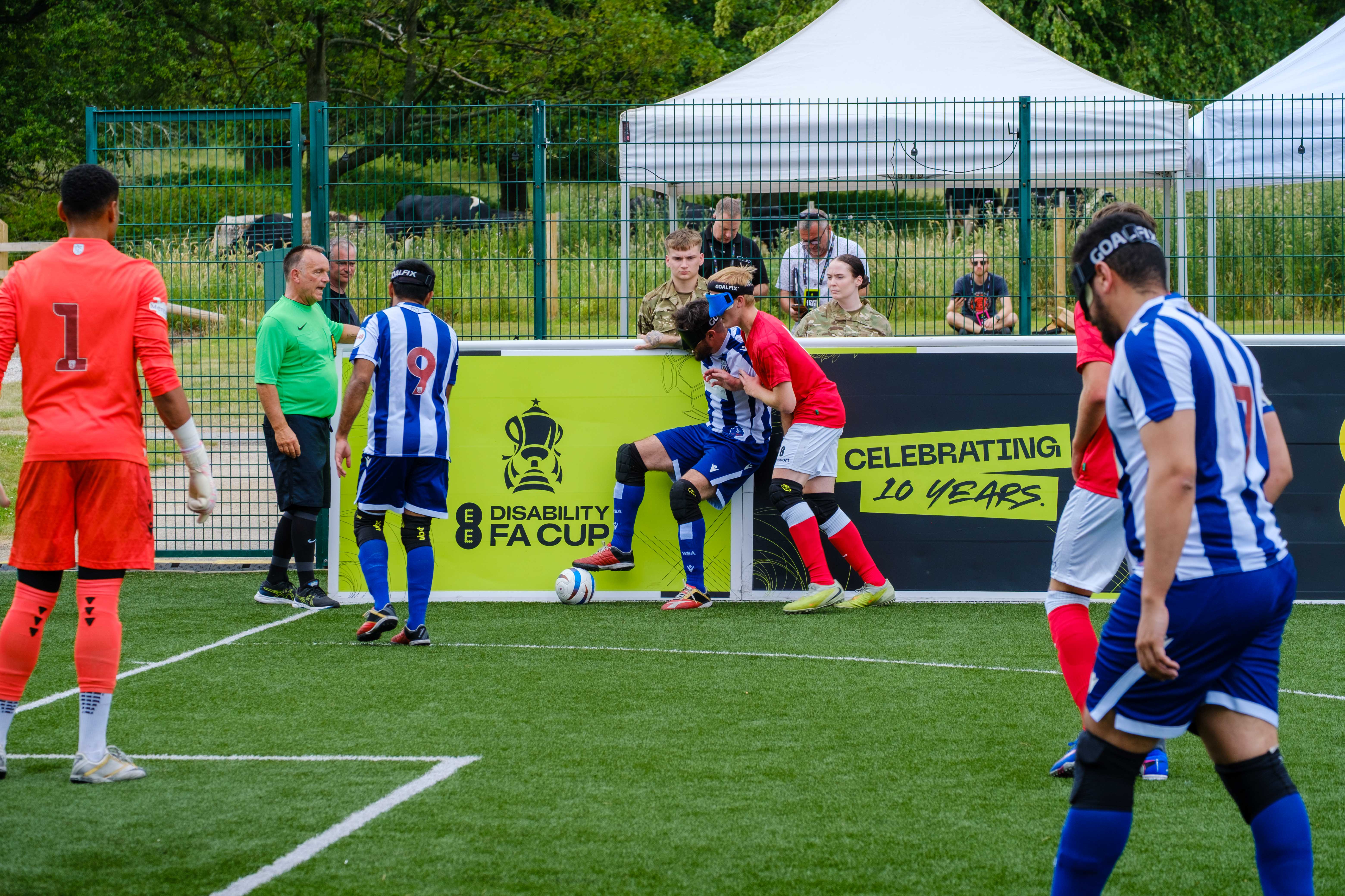 Eesa battling for the ball with a RNC player applying pressure. Players from both teams in the distance.