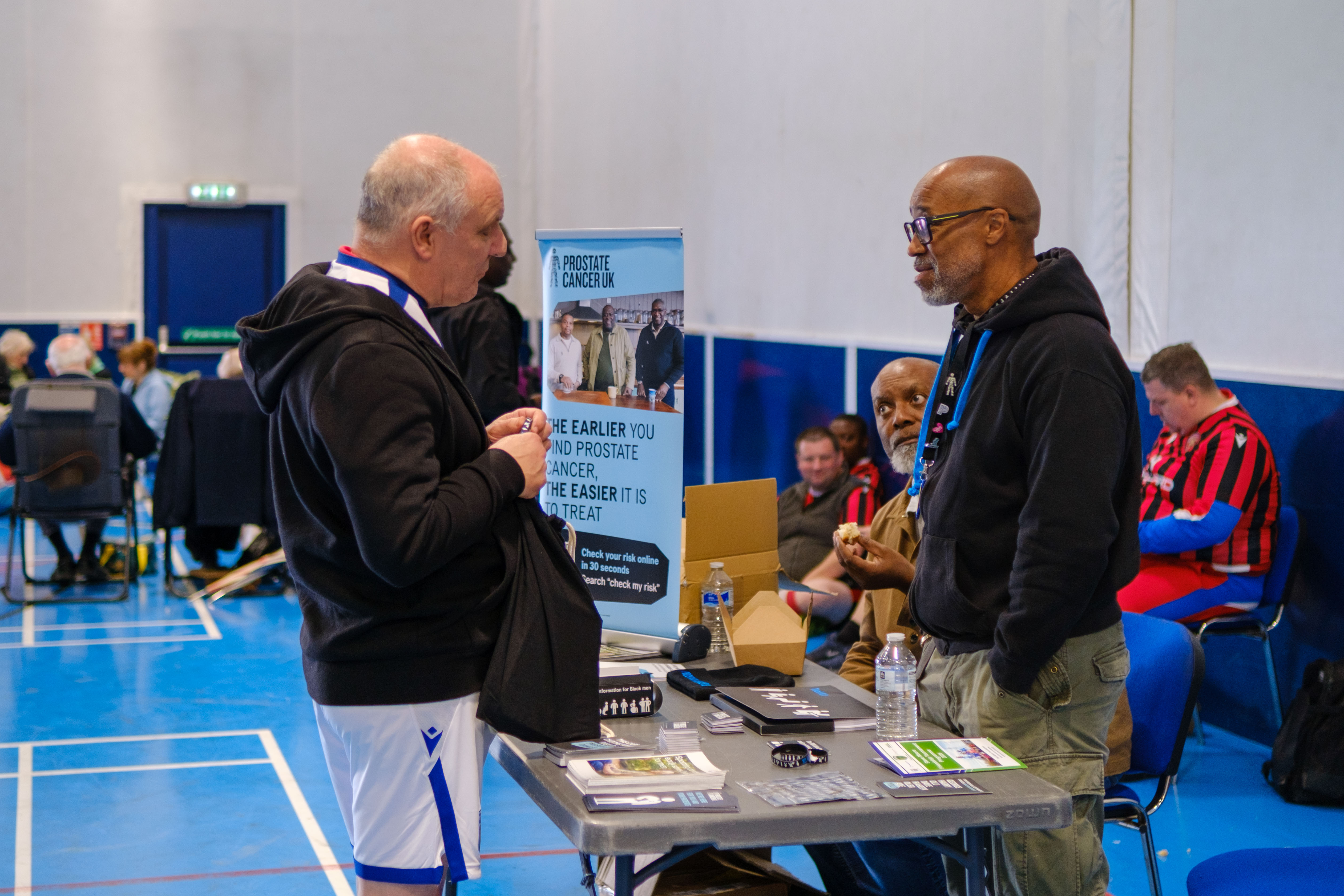 Cancer Kicker player in discussion with Prostate Cancer UK representative at the stall. 