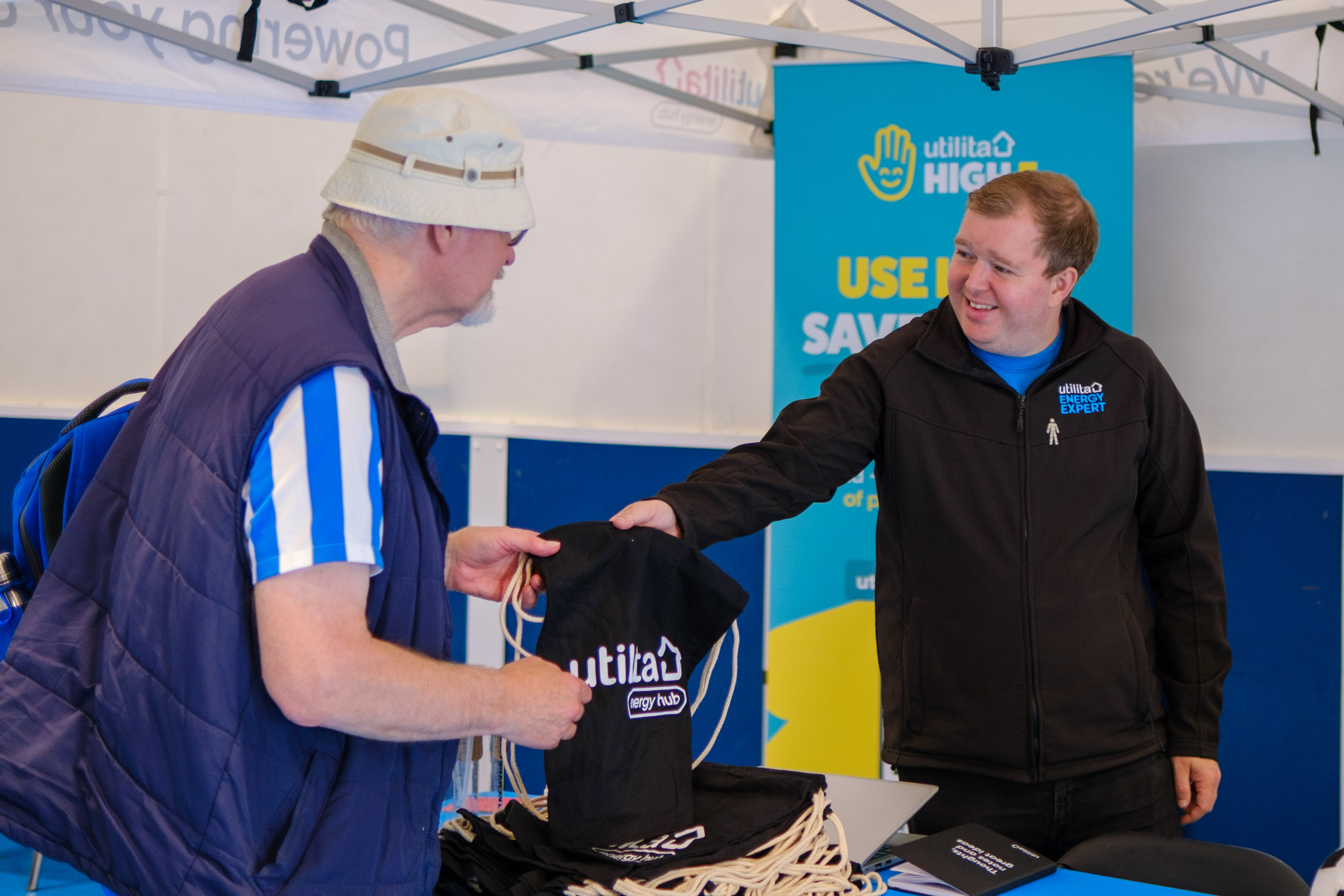 Utilita representative handing a drawstring bag to a participant at the stall. 