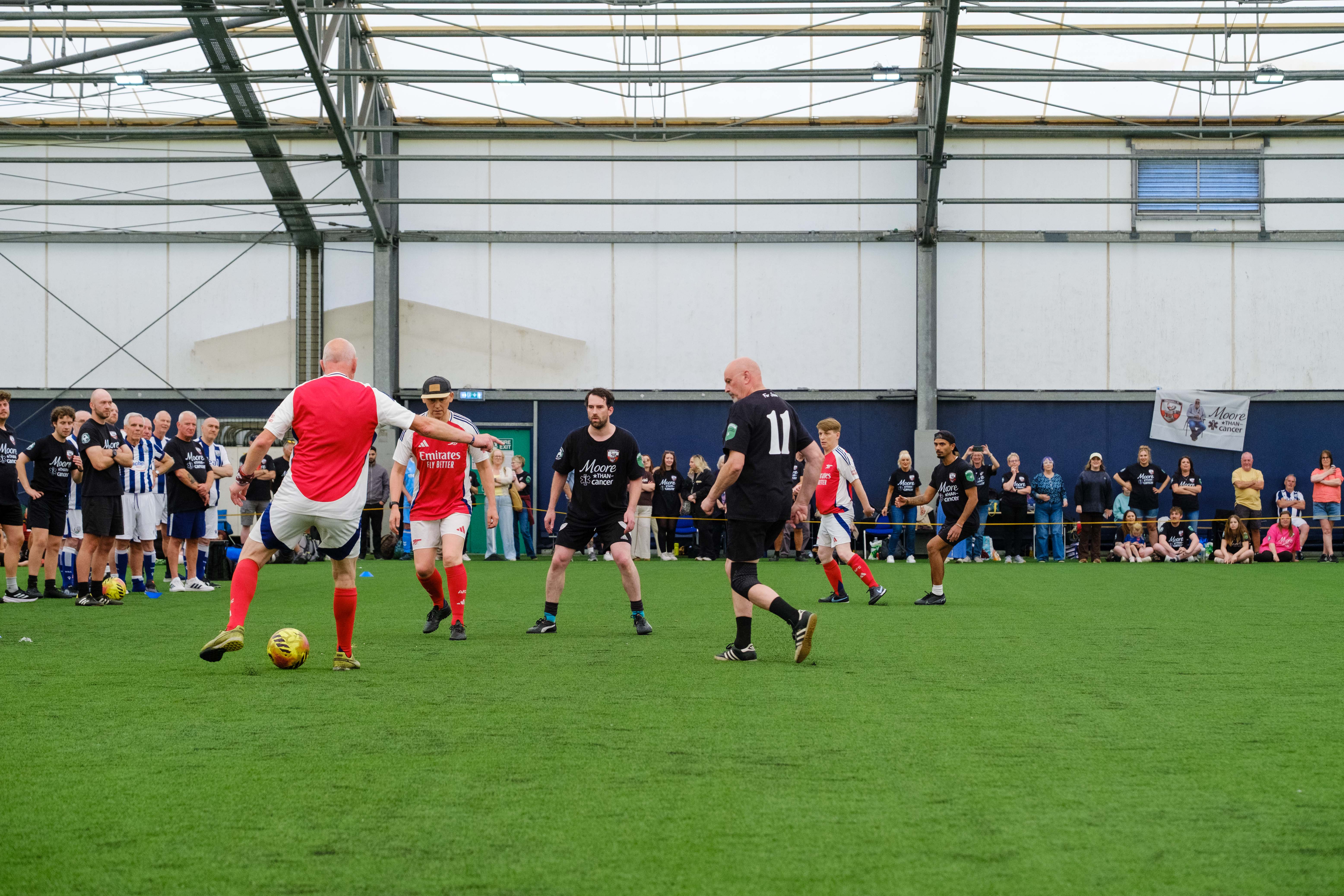 Wide shot of Moore than Cancer and Arsenal players in action with spectators on the sidelines.