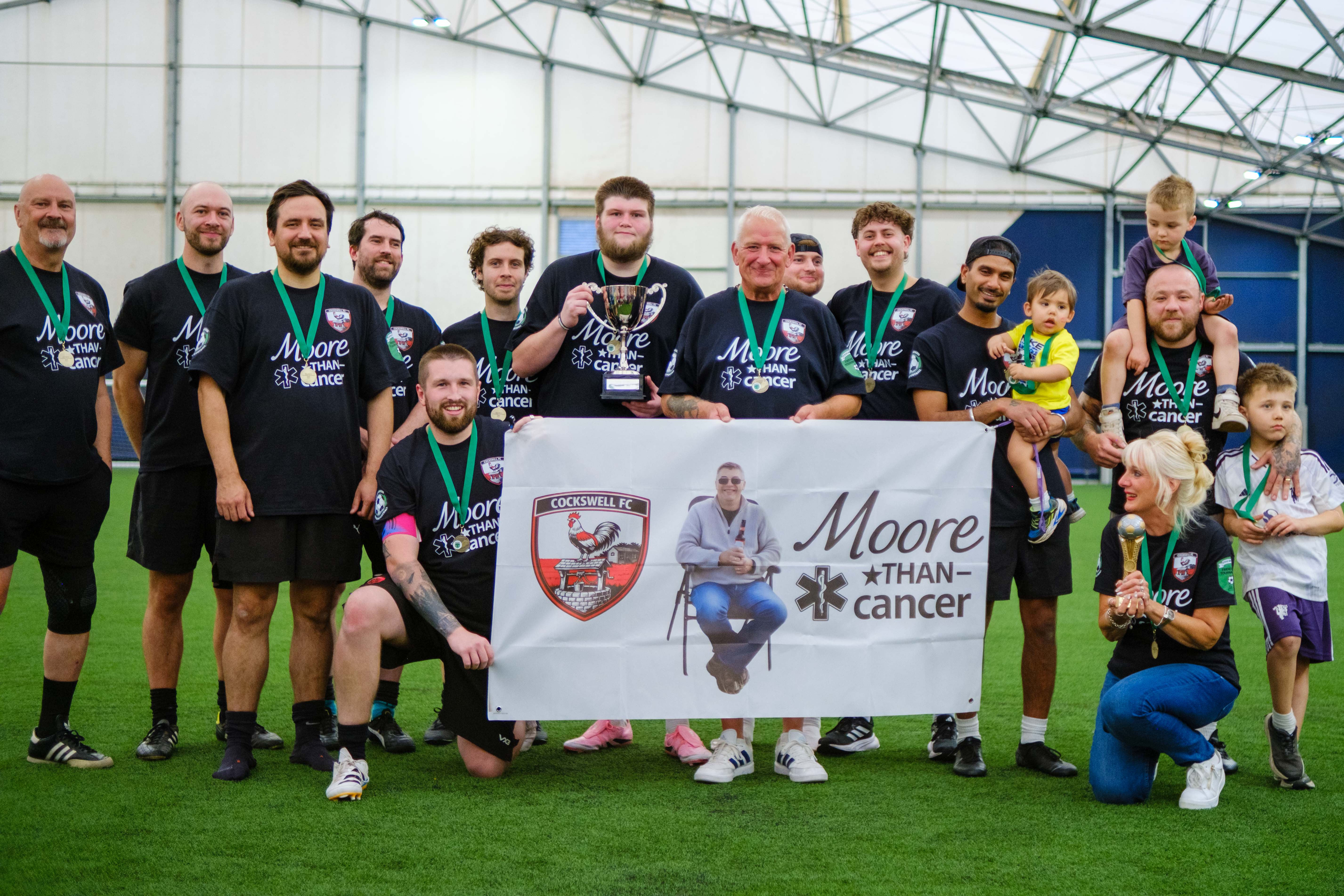 Moore than Cancer with trophy in front of tribute banner.