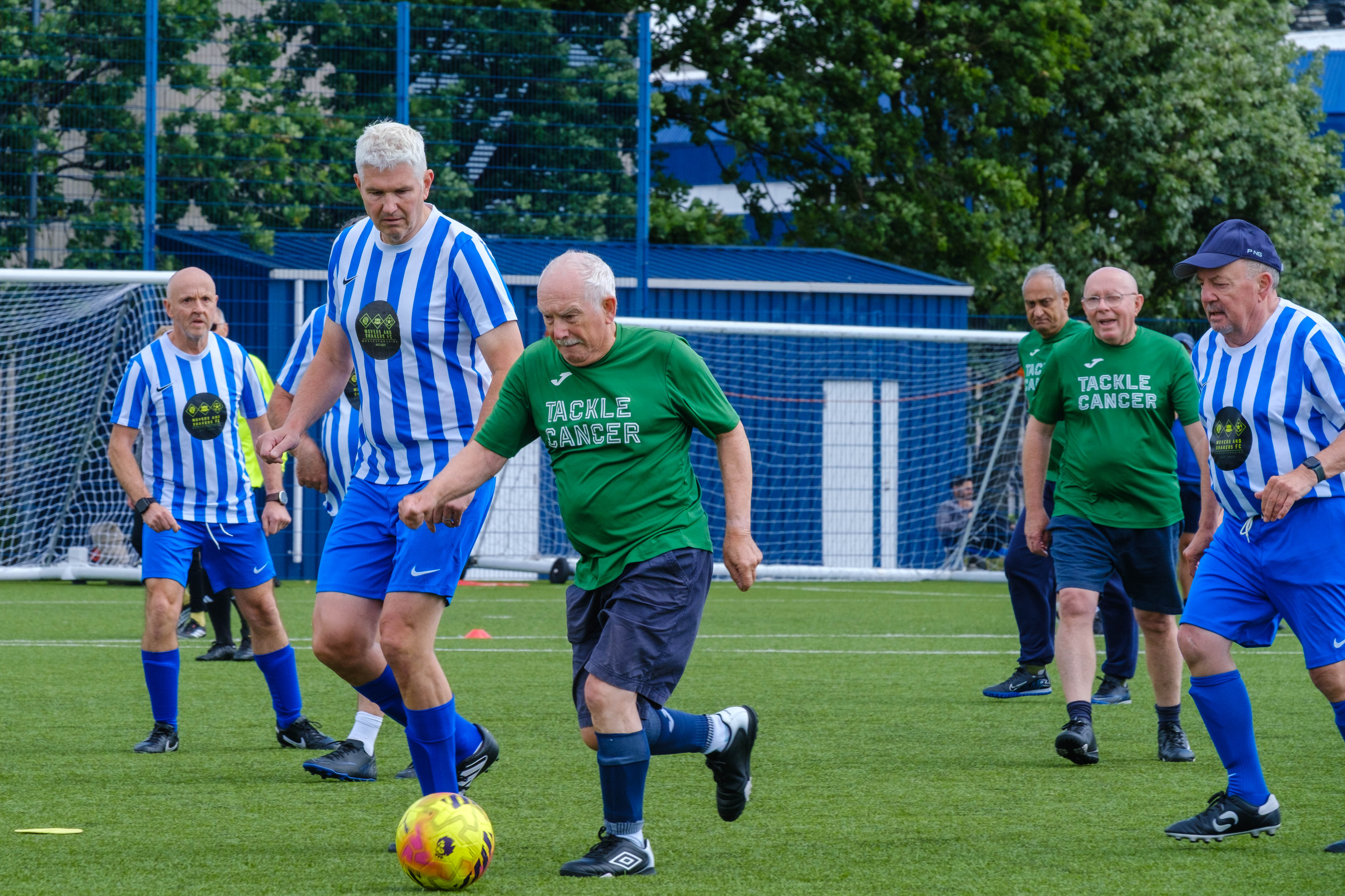 Wide shot of Big C tackling Cancer and Movers and Shakers on the pitch chasing the ball