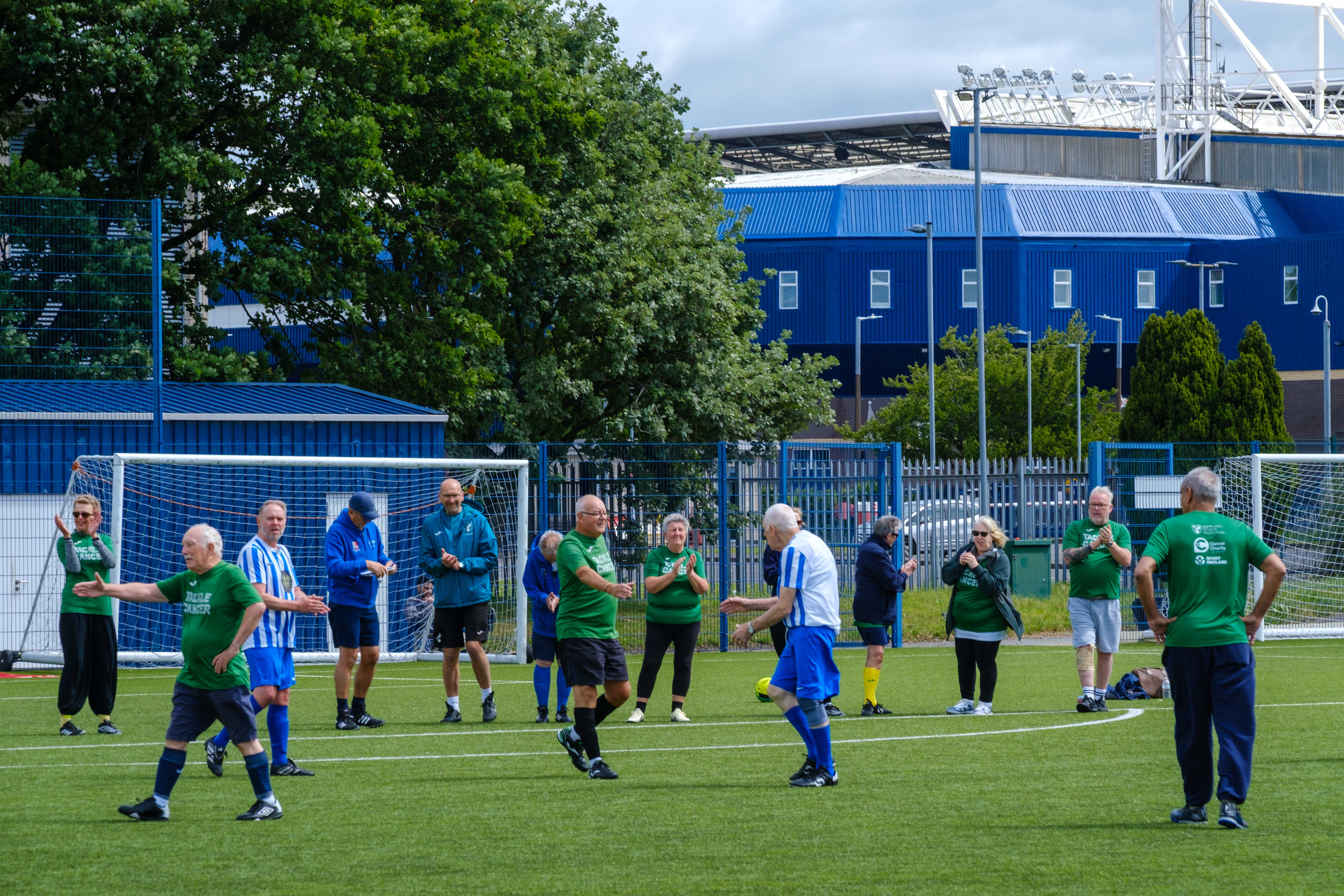 Wide shot of Big C tackling Cancer and Movers and Shakers shaking hands with The Hawthorns in the background.