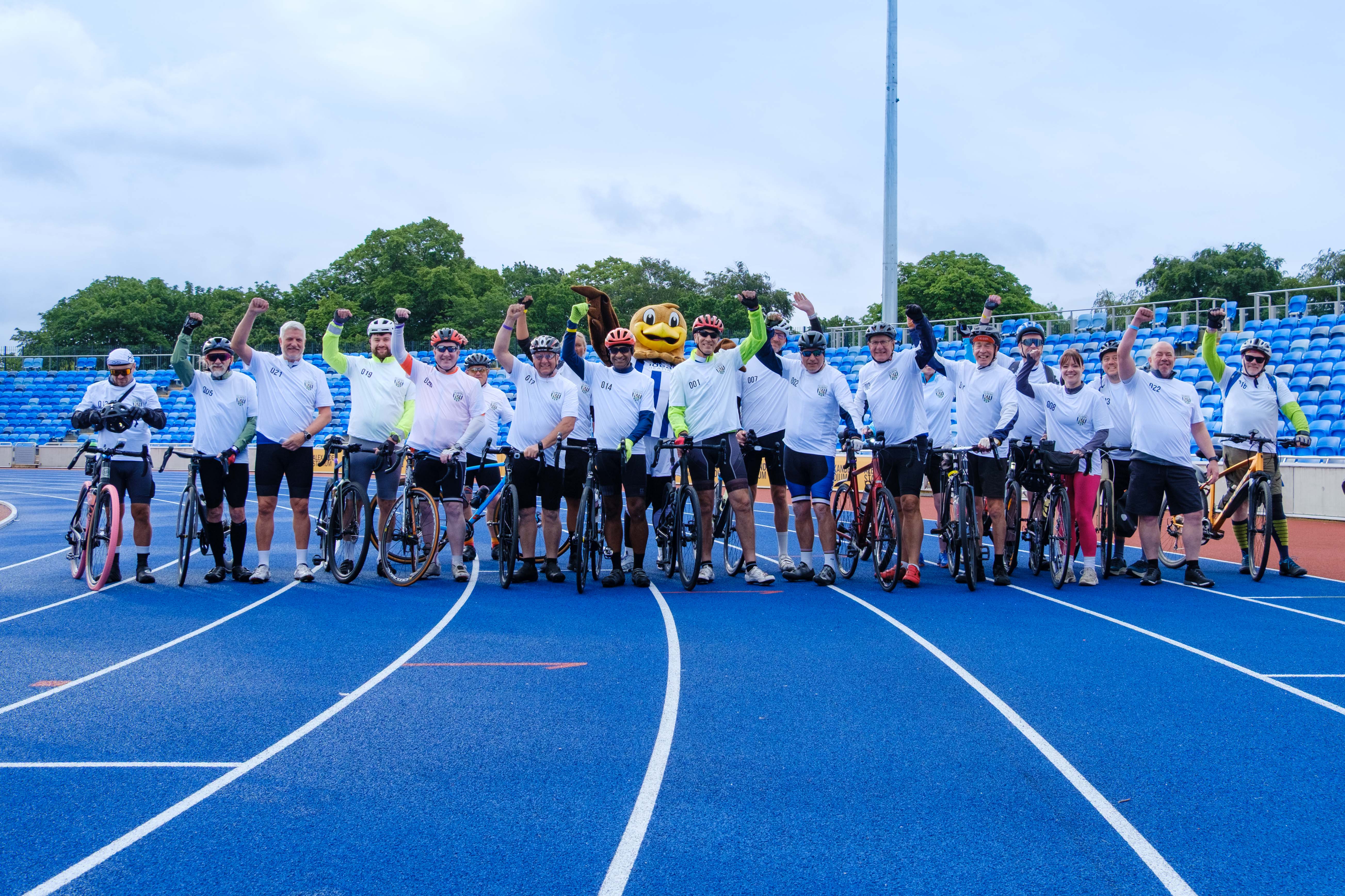 The Albion Foundation cyclists group photo, holding bikes on the Alexander Stadium running track.