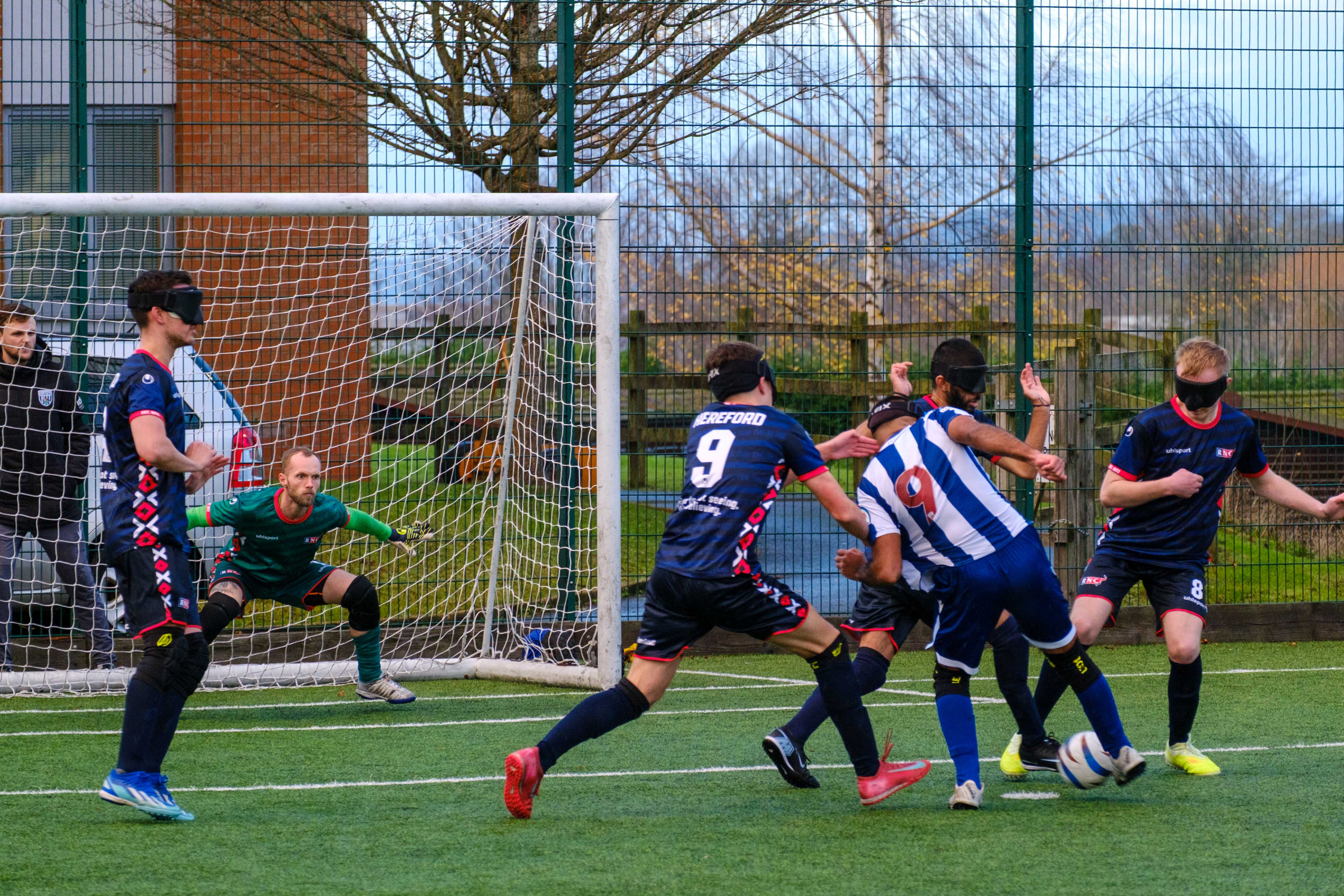 Three RNC players surrounding Eesa with the goalkeeper in a stance ready to make a save.