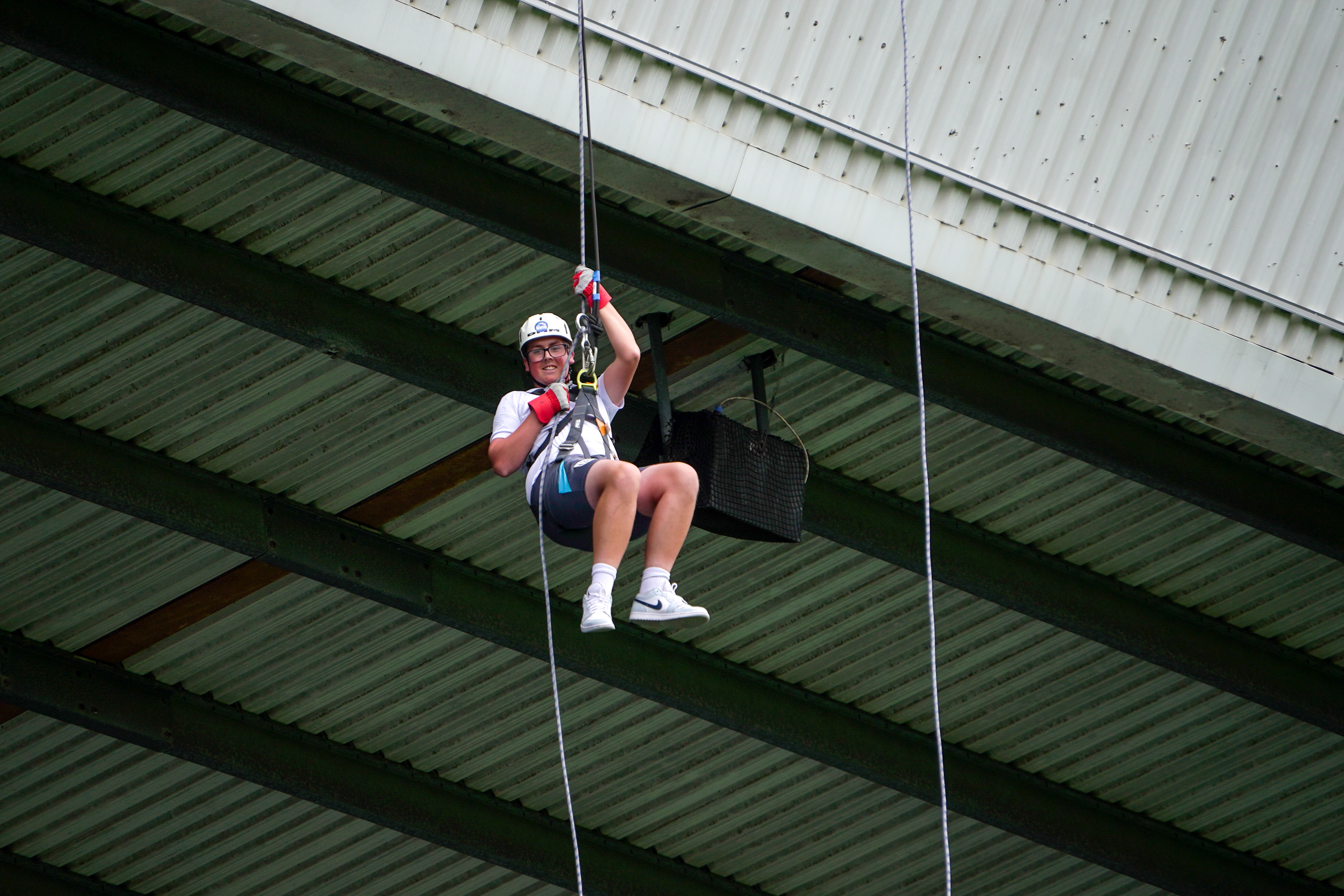 Participant wearing a helmet, harness and safety gloves abseils from the roof of The Hawthorns, suspended on ropes beneath the stadium structure.