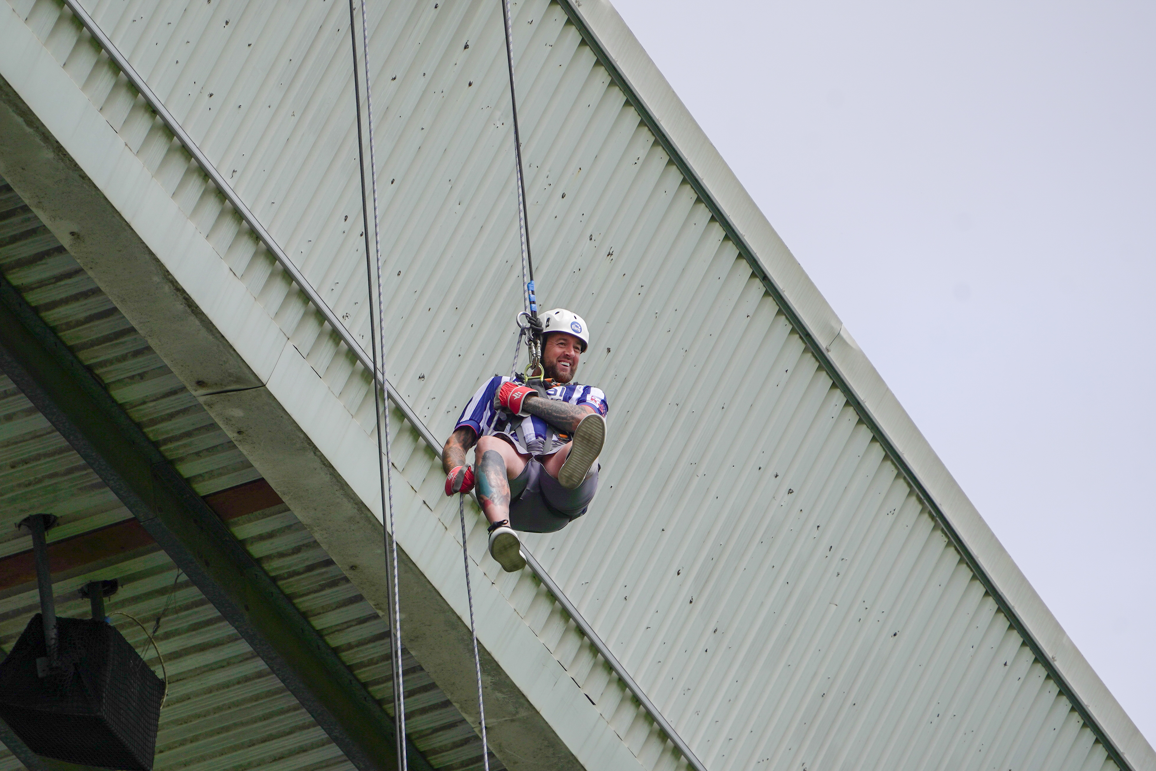 Participant wearing a helmet, harness and safety gloves abseils from the roof of The Hawthorns during a charity abseil event.