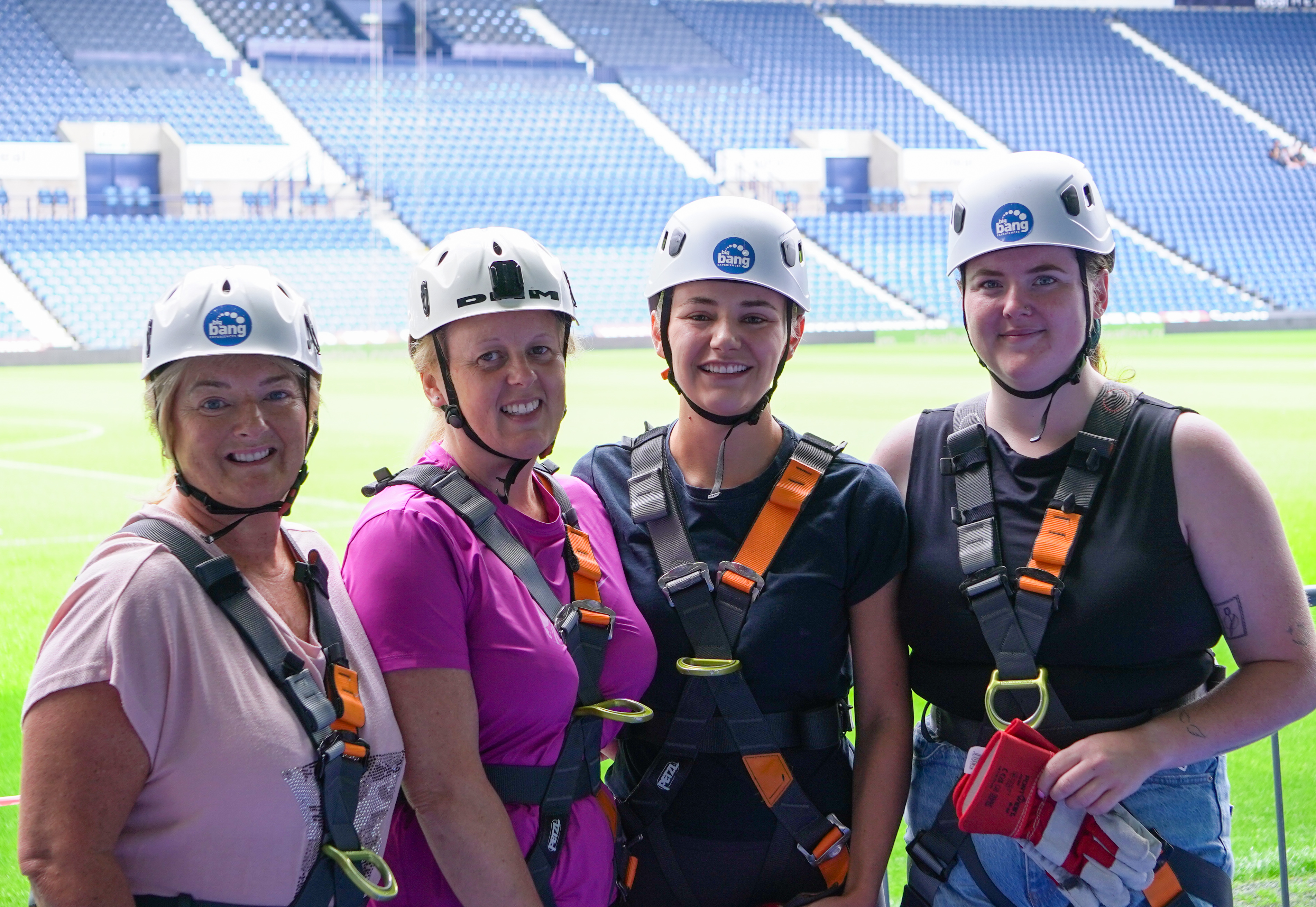 Four participants wearing helmets and safety harnesses pose for a photo at The Hawthorns, with the pitch and stadium seating visible behind them.