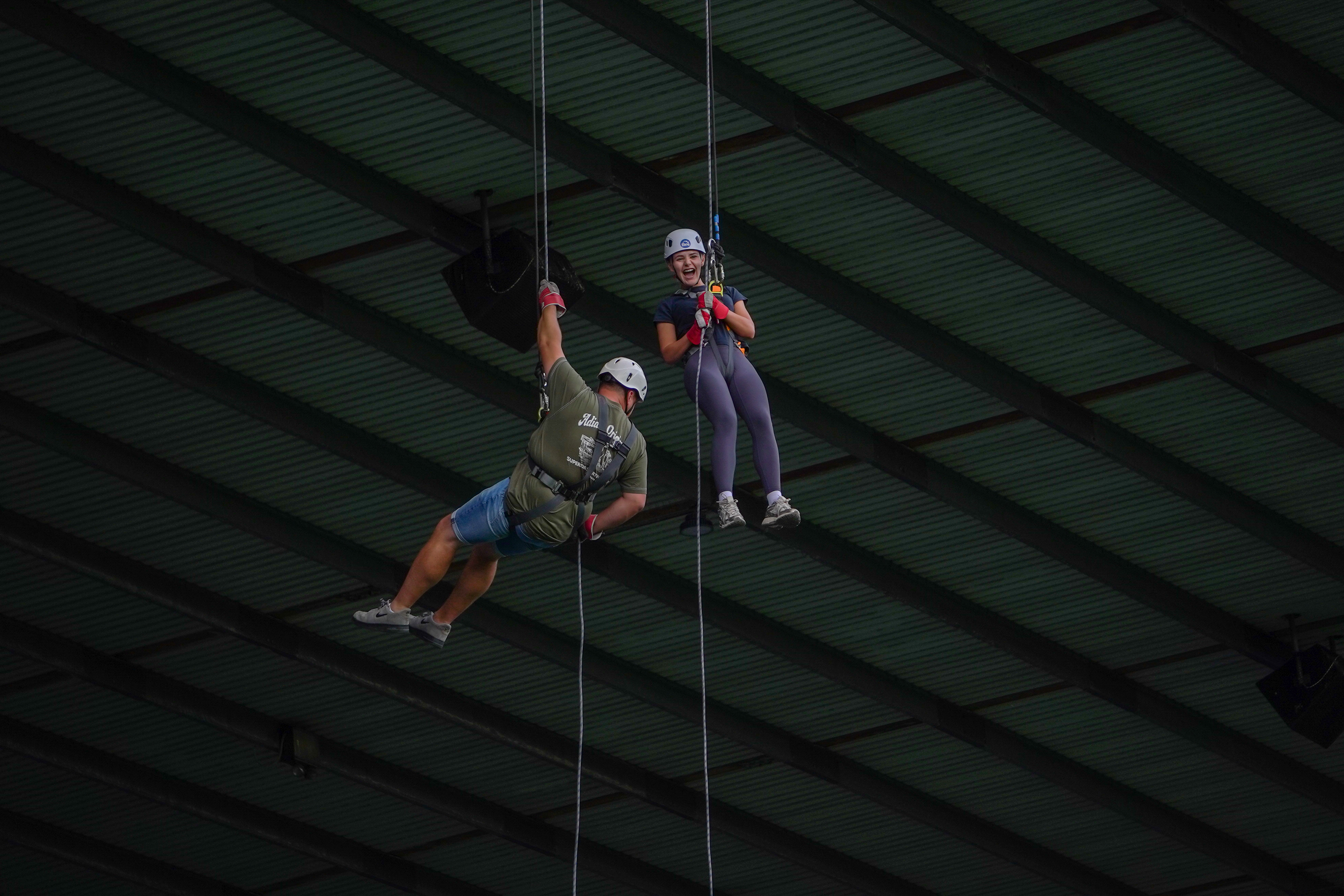 Two participants wearing helmets and harnesses abseil side by side beneath the stadium roof during a charity abseil event at The Hawthorns.