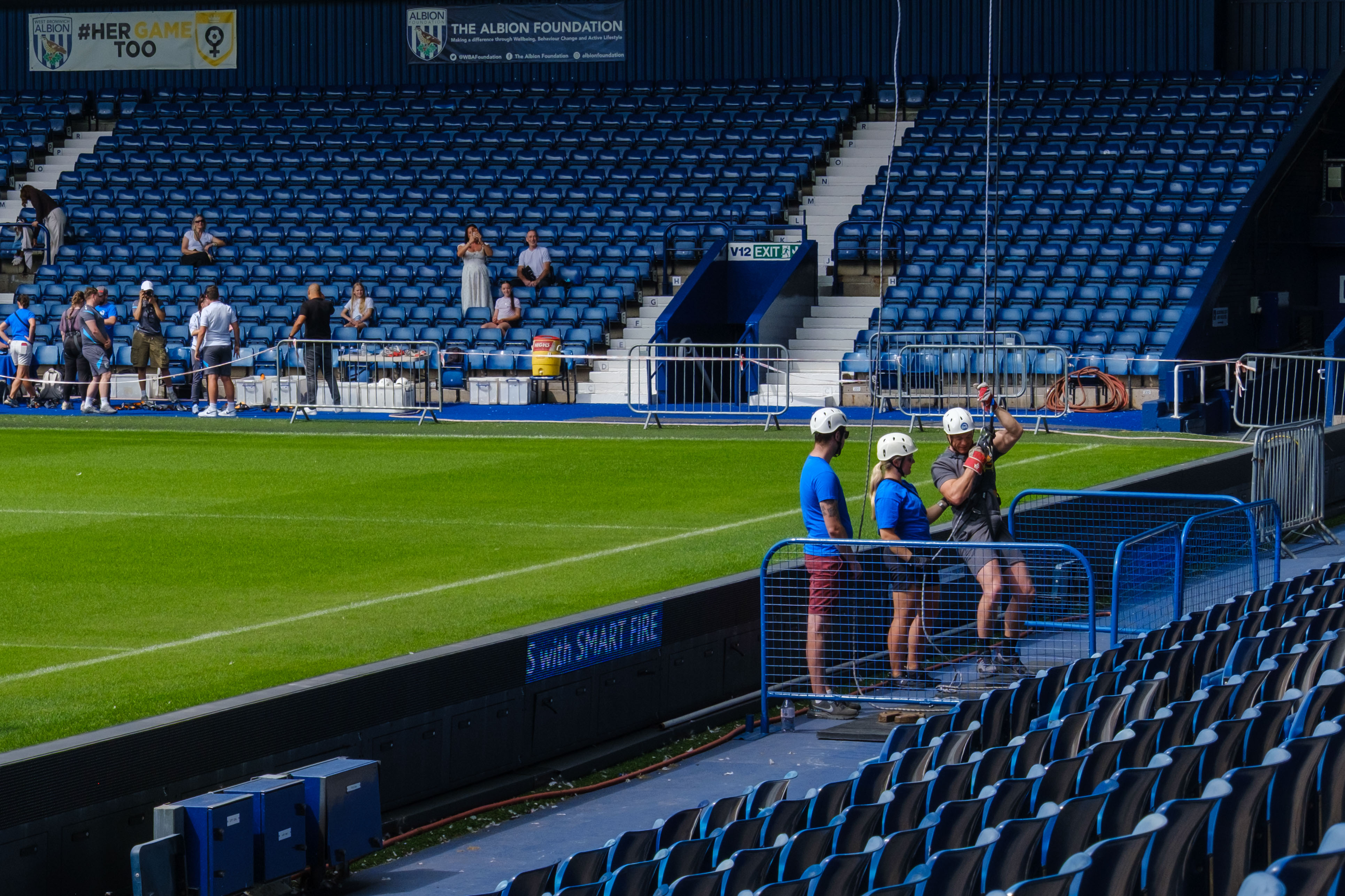 Participant completes an abseil at pitchside at The Hawthorns, with support staff, spectators and rows of blue seats visible in the background.Provide your feedback on BizChatAdd alt text for the next imageDescribe the abseiling setupWhat safety checks are visible?FilesFiles