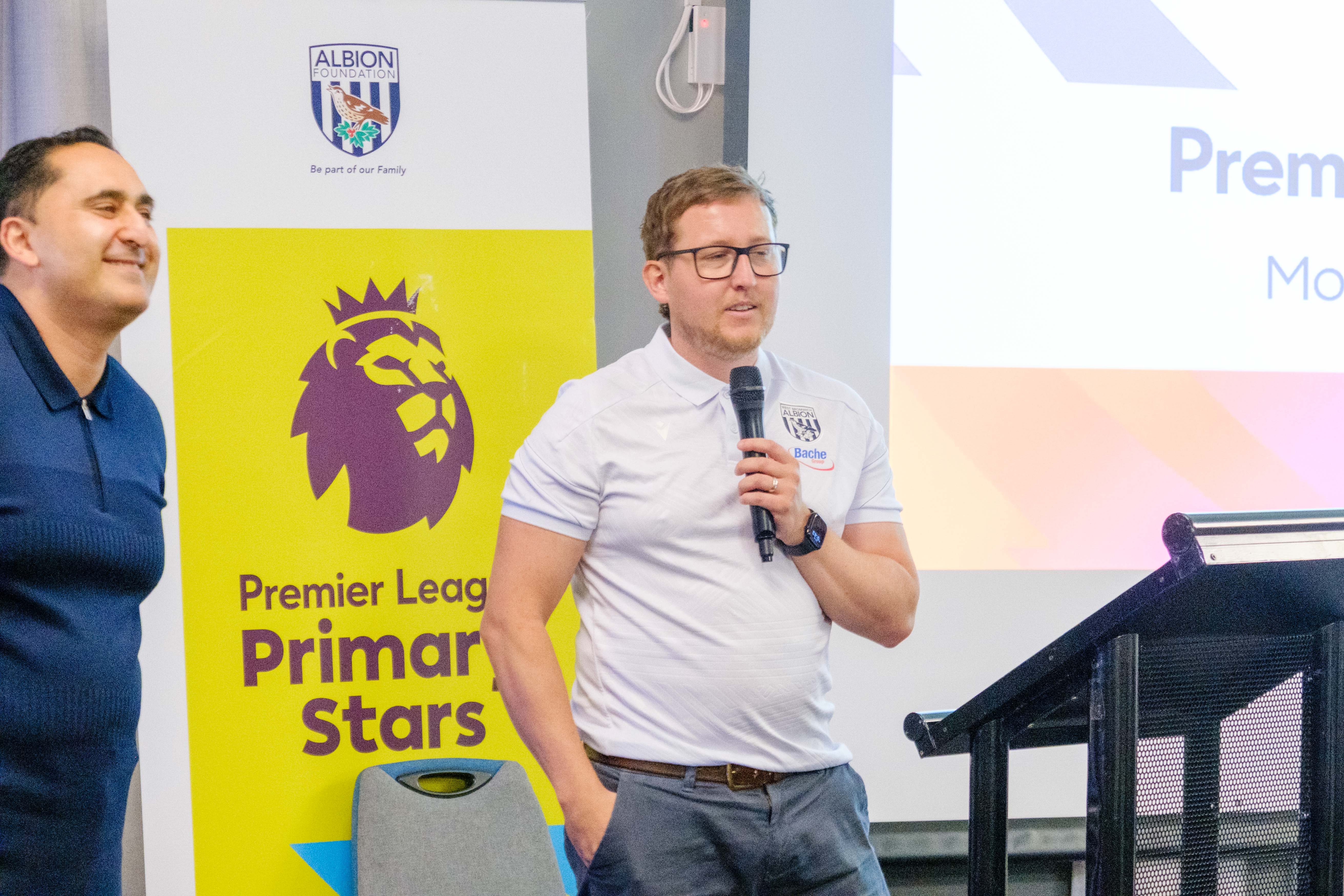 Deputy Director Jon Ward speaking on the mic at the front of the room with Rupi Lal at the side. 