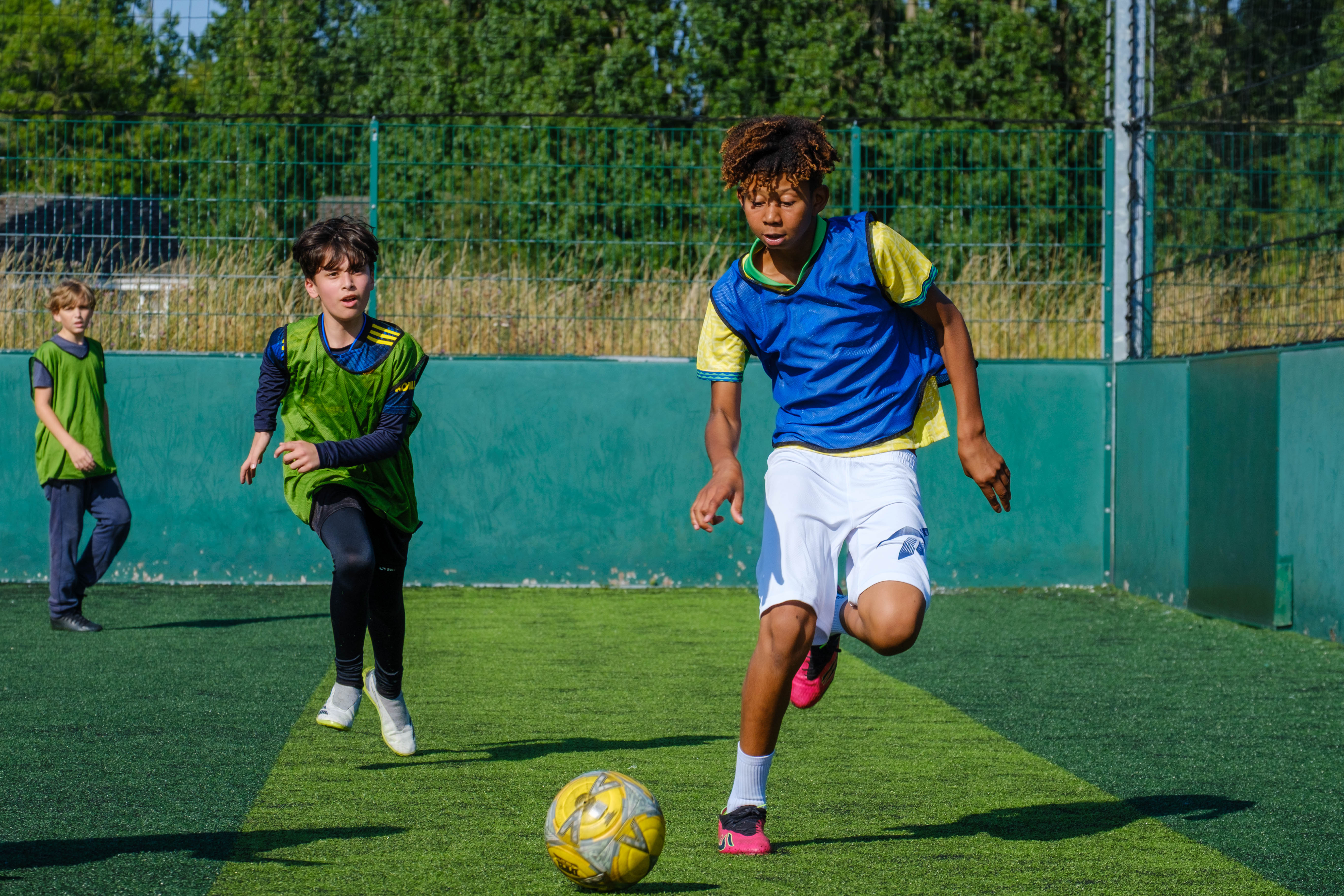 Premier League Kicks participants compete for the ball during a match on an outdoor artificial pitch.