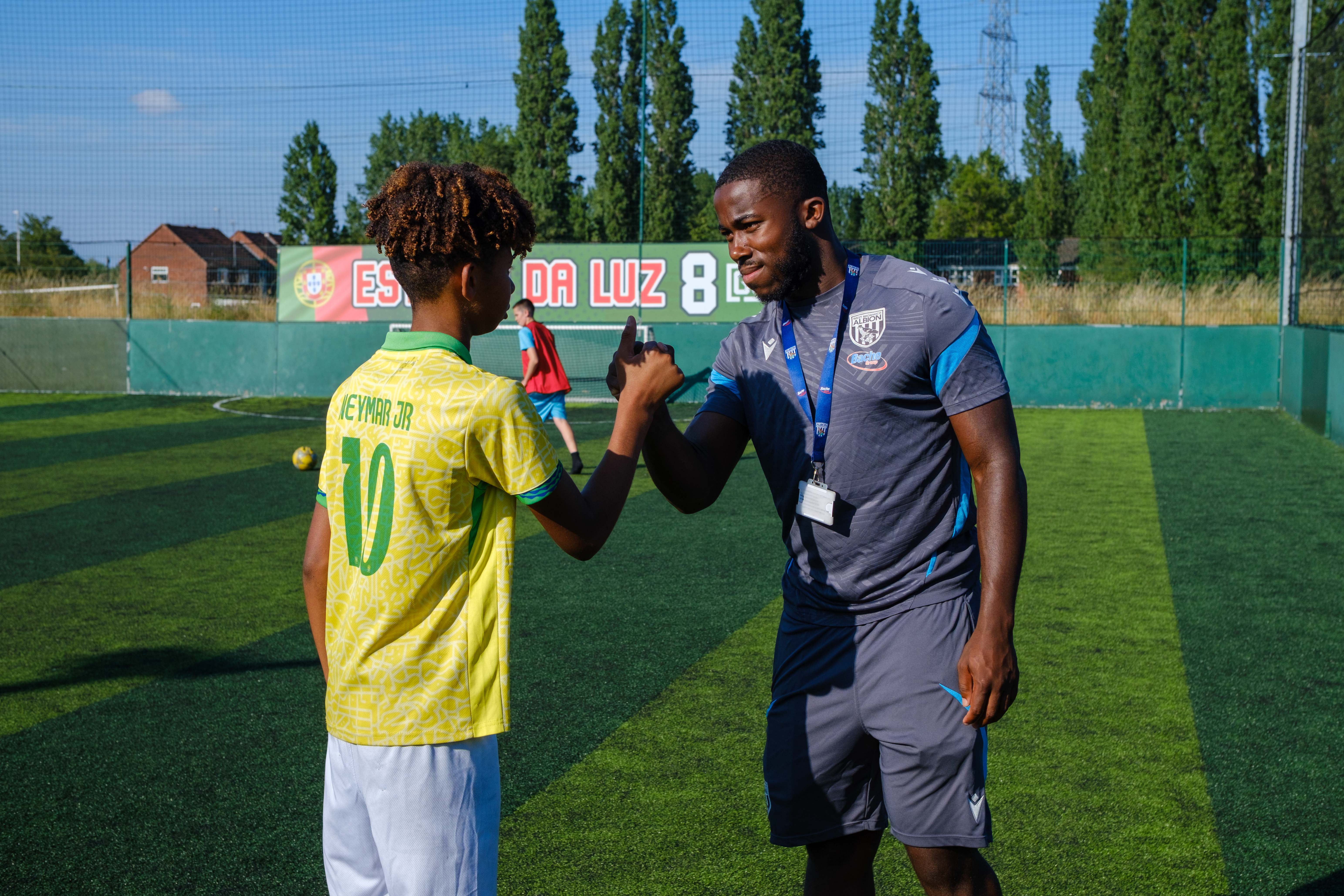 Premier League Kicks coach and participant exchange a hand shake on an outdoor football pitch following a session.
