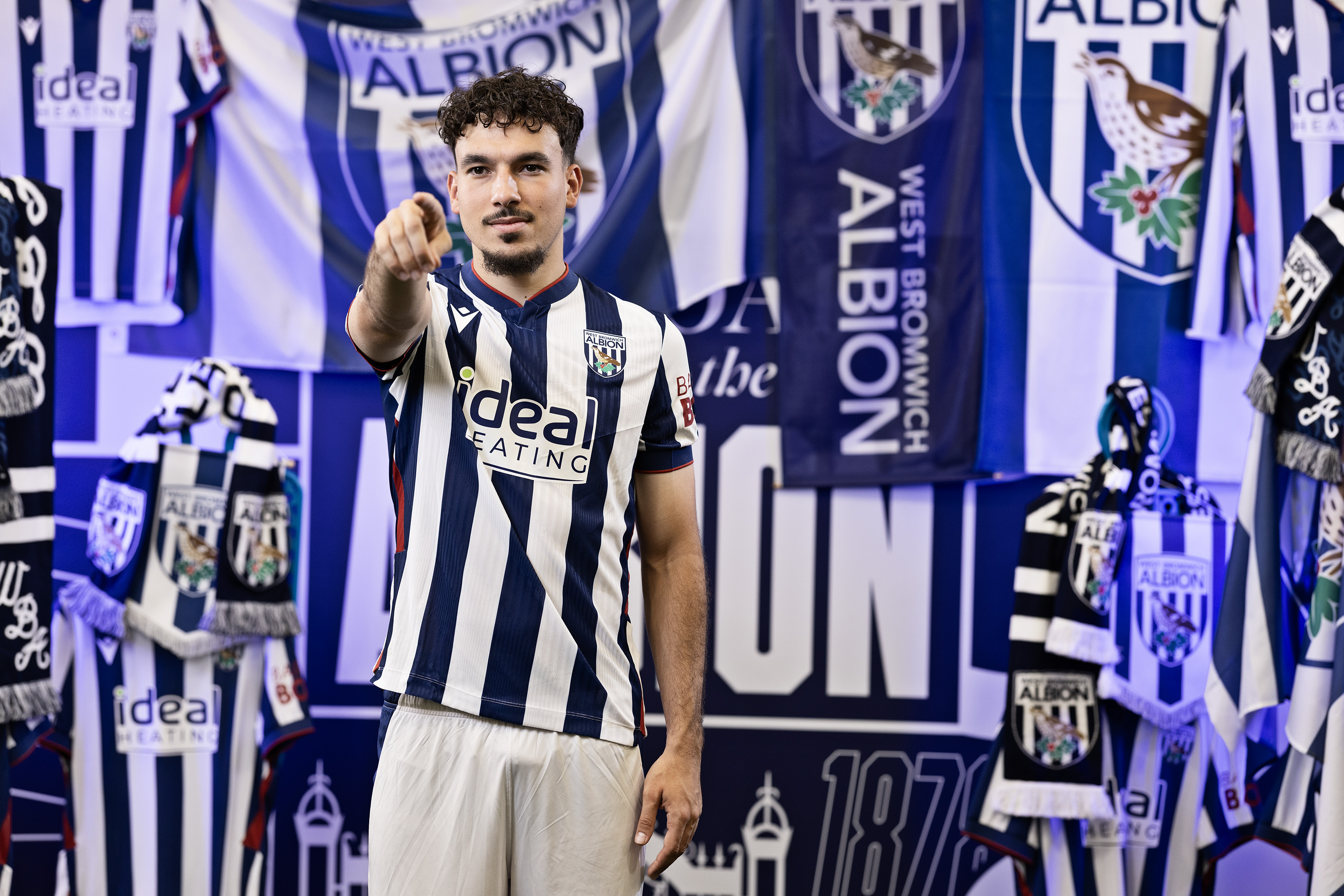 Nolan Galves in the home shirt pointing at the camera while stood in front of heavy WBA branding
