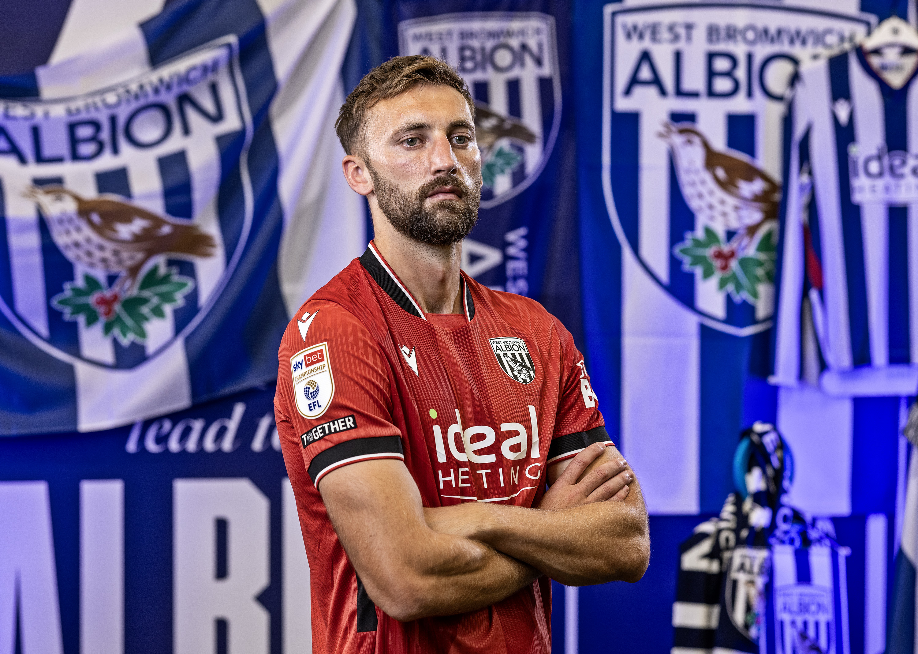 Nat Phillips in the away kit with his arms crossed looking at the camera in front of WBA branding 