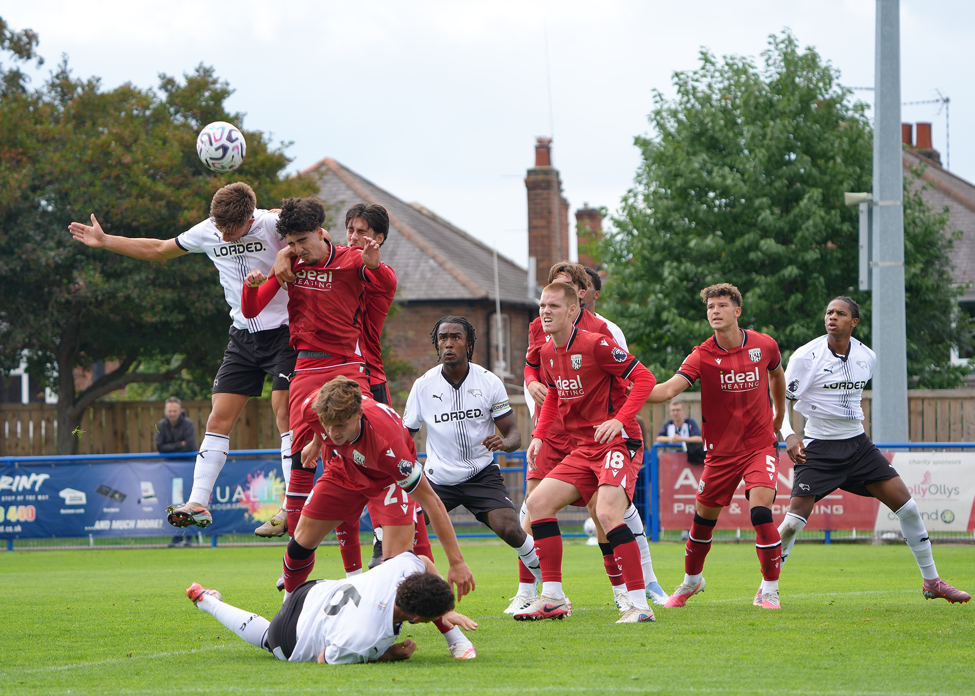General match action with the ball in the air and several Derby PL2 and WBA players challenging to win it 