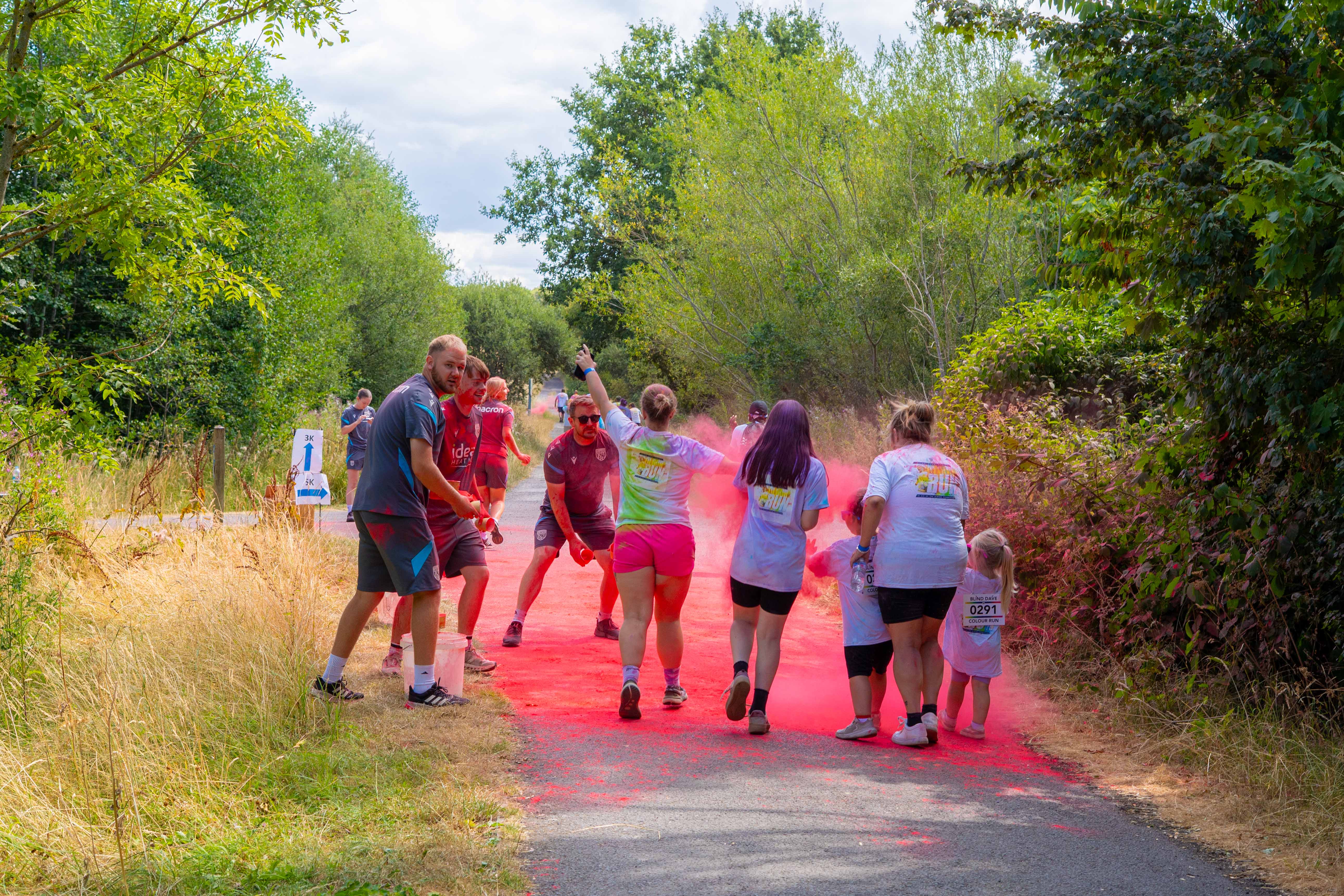 Participants walk through a cloud of pink color powder on a path.