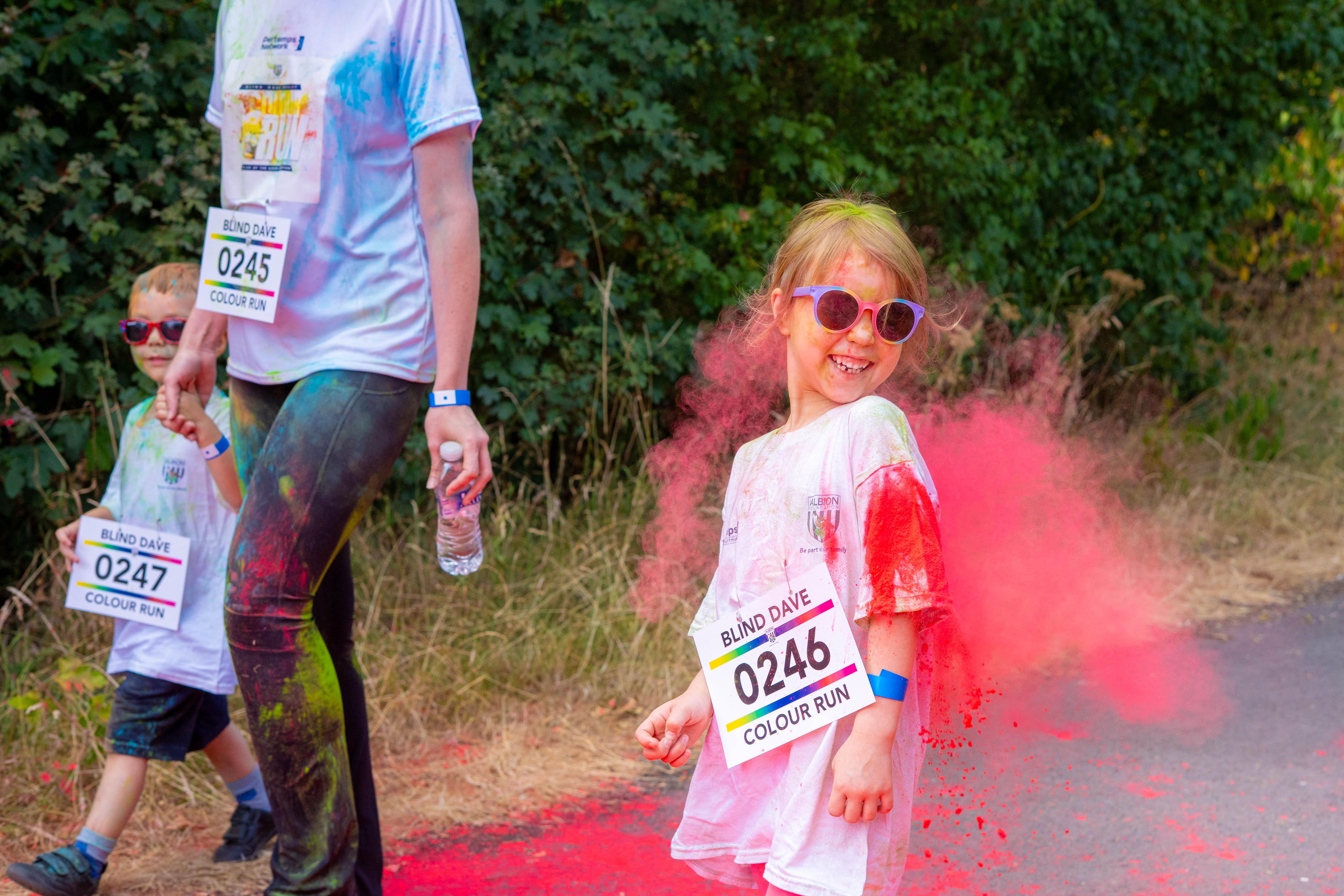 A child participant walks beside an adult while covered in pink powder.