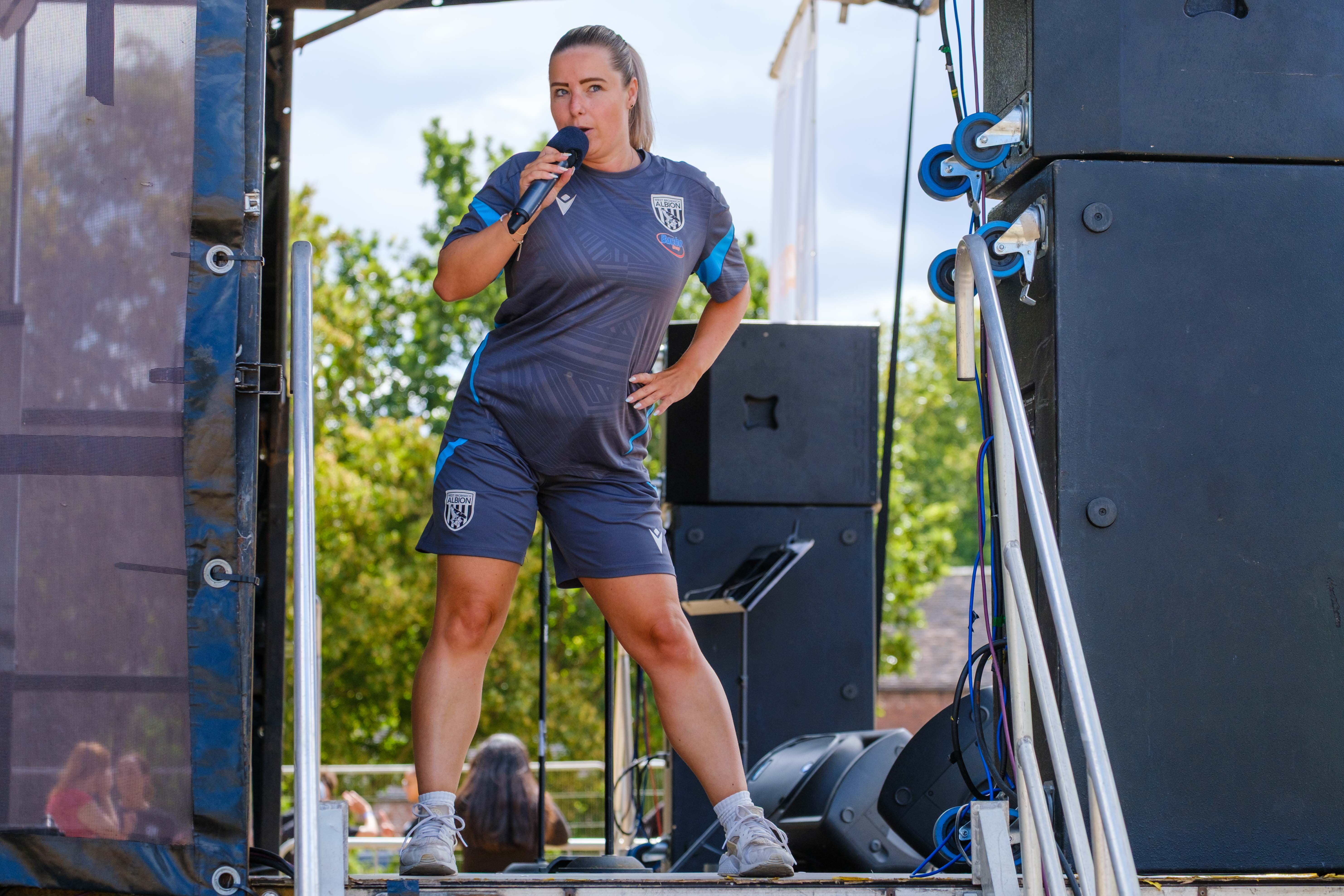 Albion Foundation staff member leads a warm-up from the event stage using a microphone before the charity colour run.