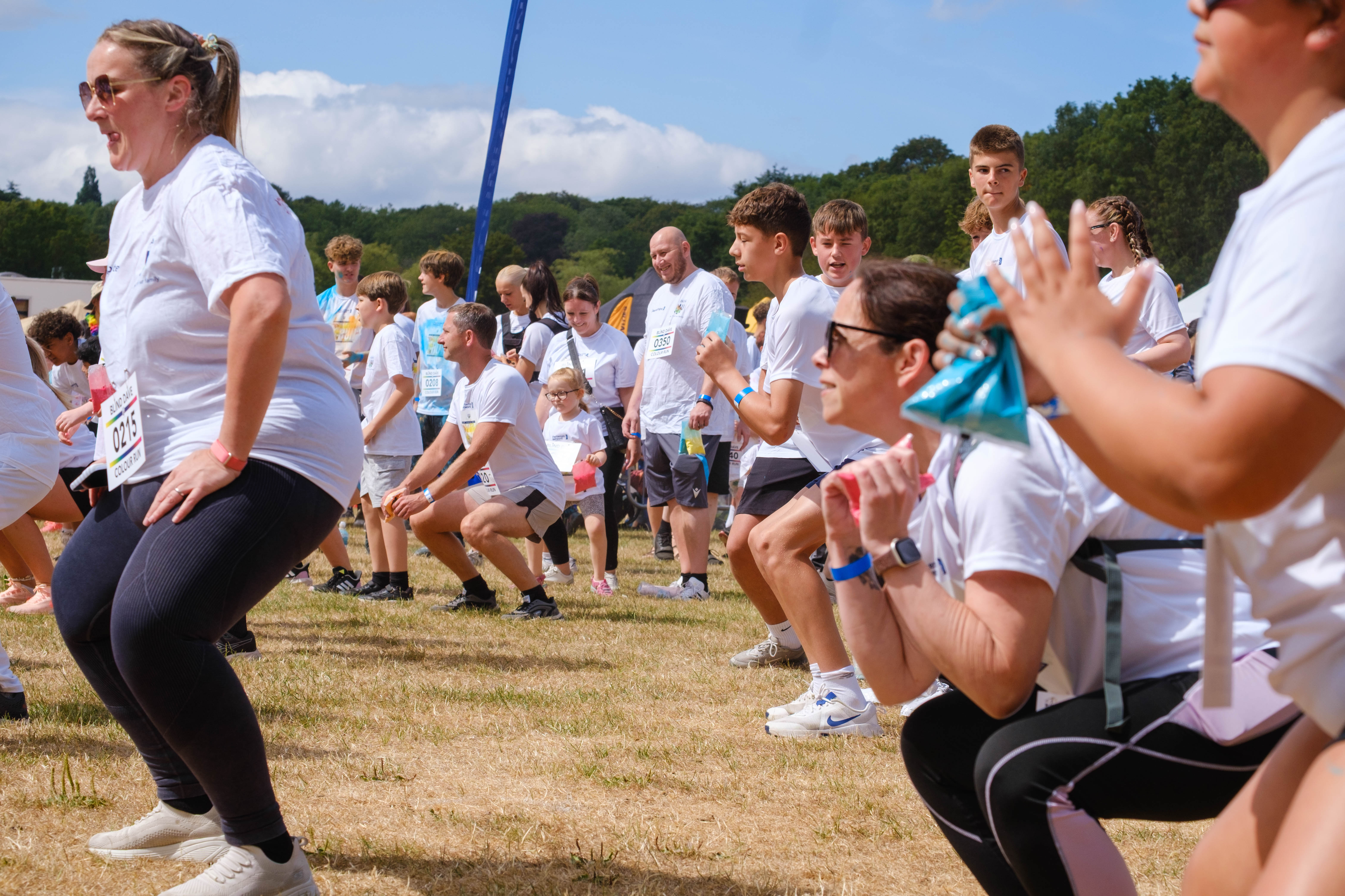 Colour run participants follow a group warm-up activity on an open field, performing exercises before the event begins.