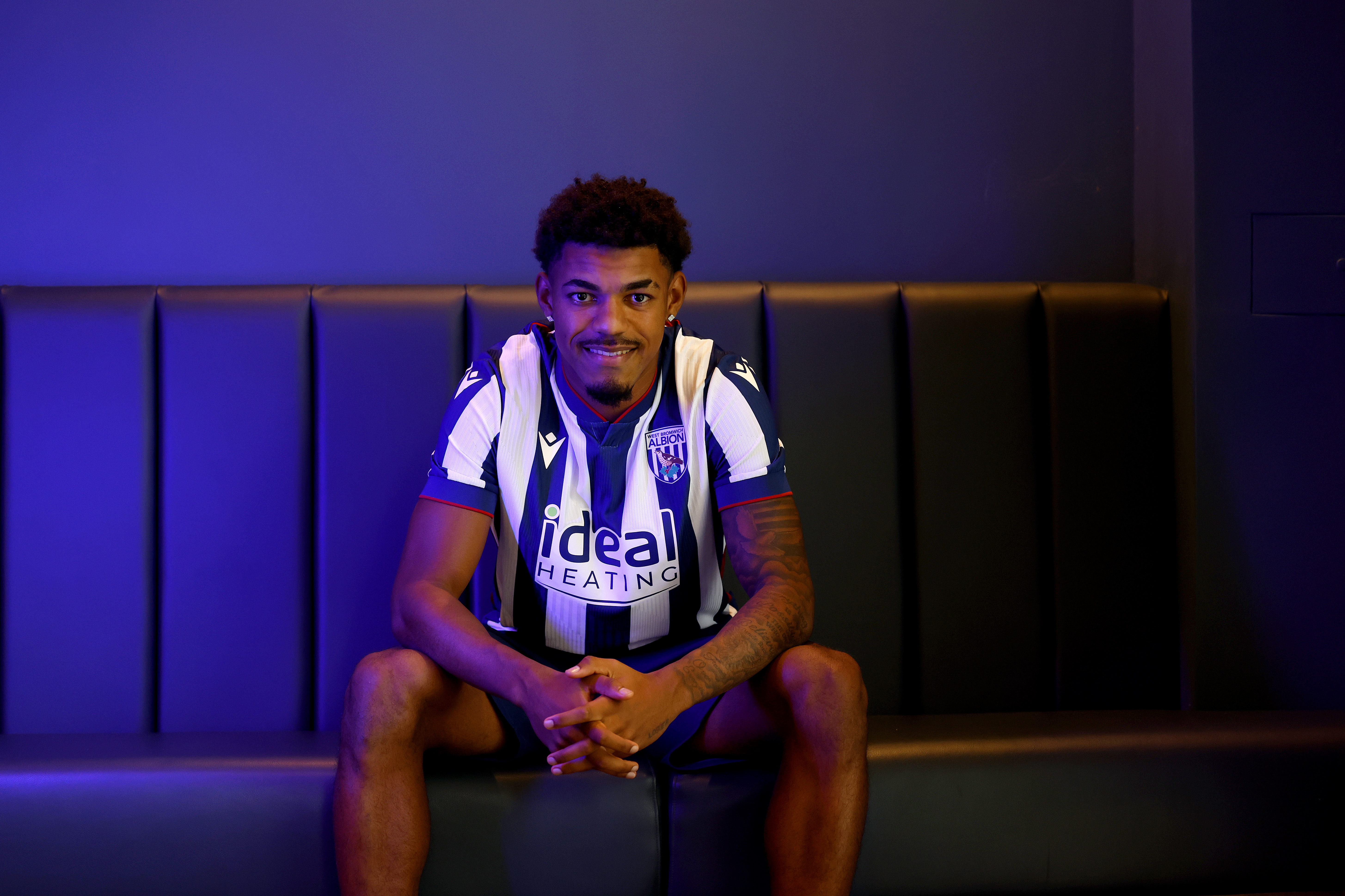 Kareem Tunde smiling at the camera while sat in a home shirt 