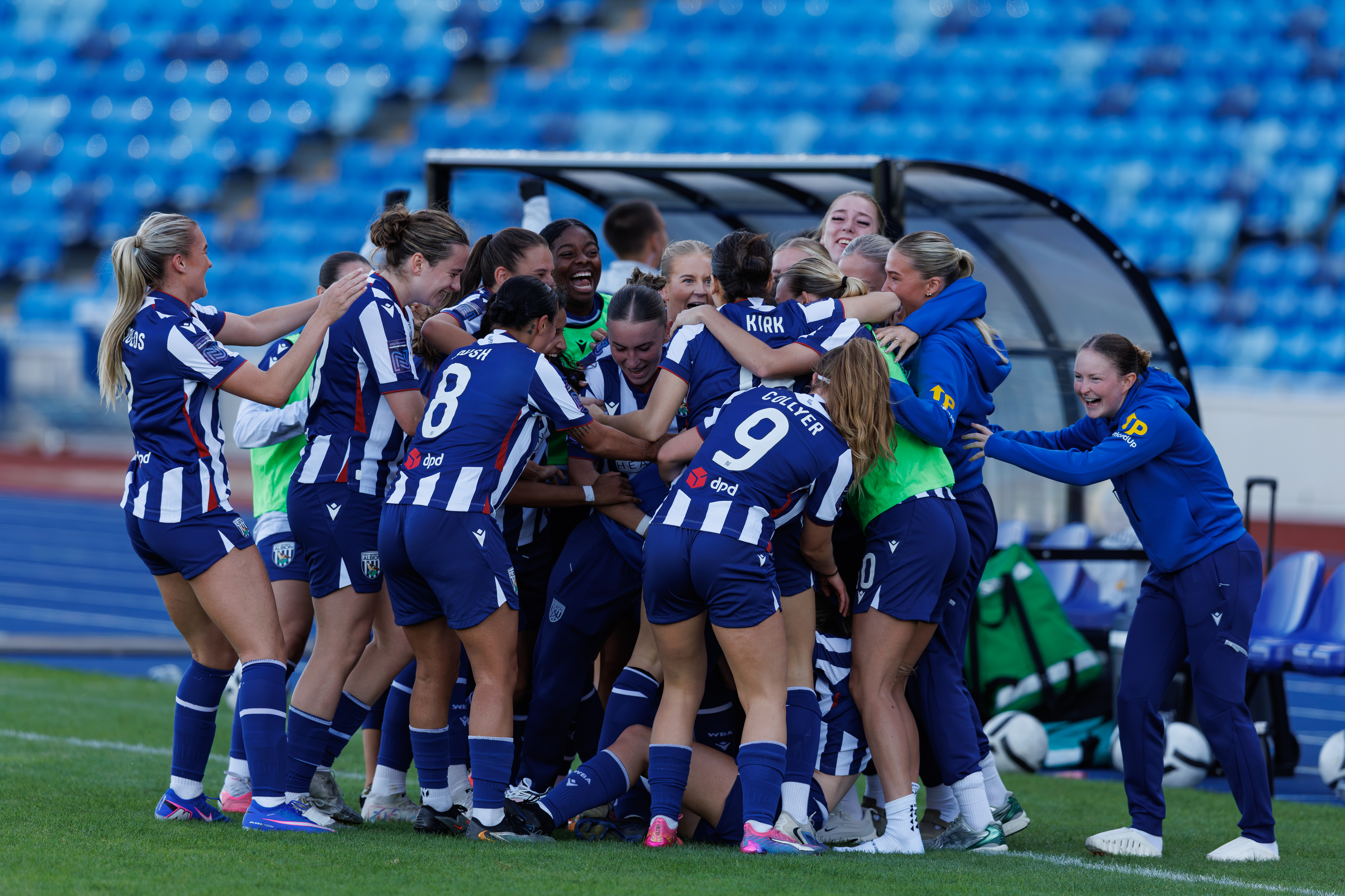 Albion Women players and staff celebrate a goal in front of a dugout 