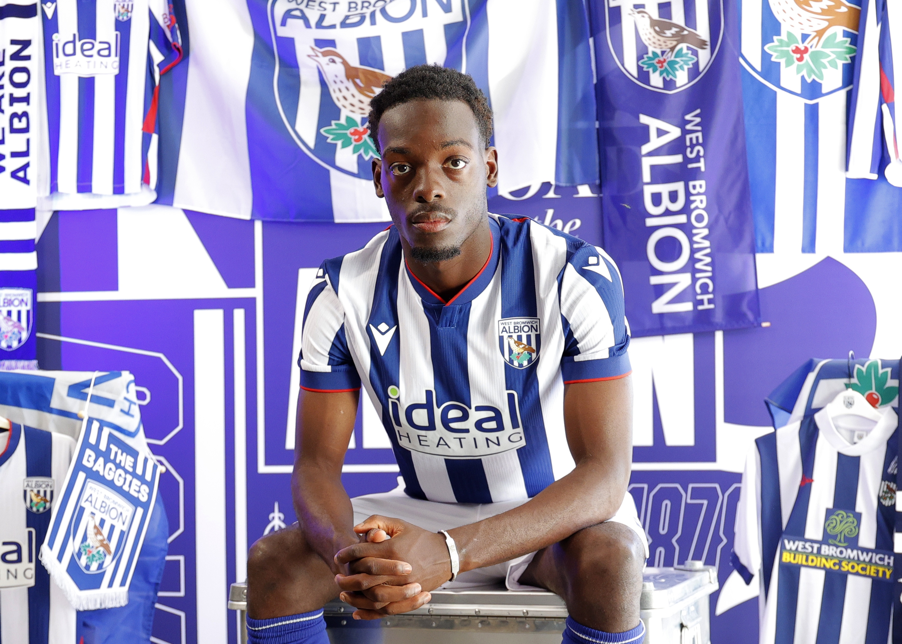 Rabby Nzingoula sat looking at the camera while in home WBA kit in front of WBA branding 