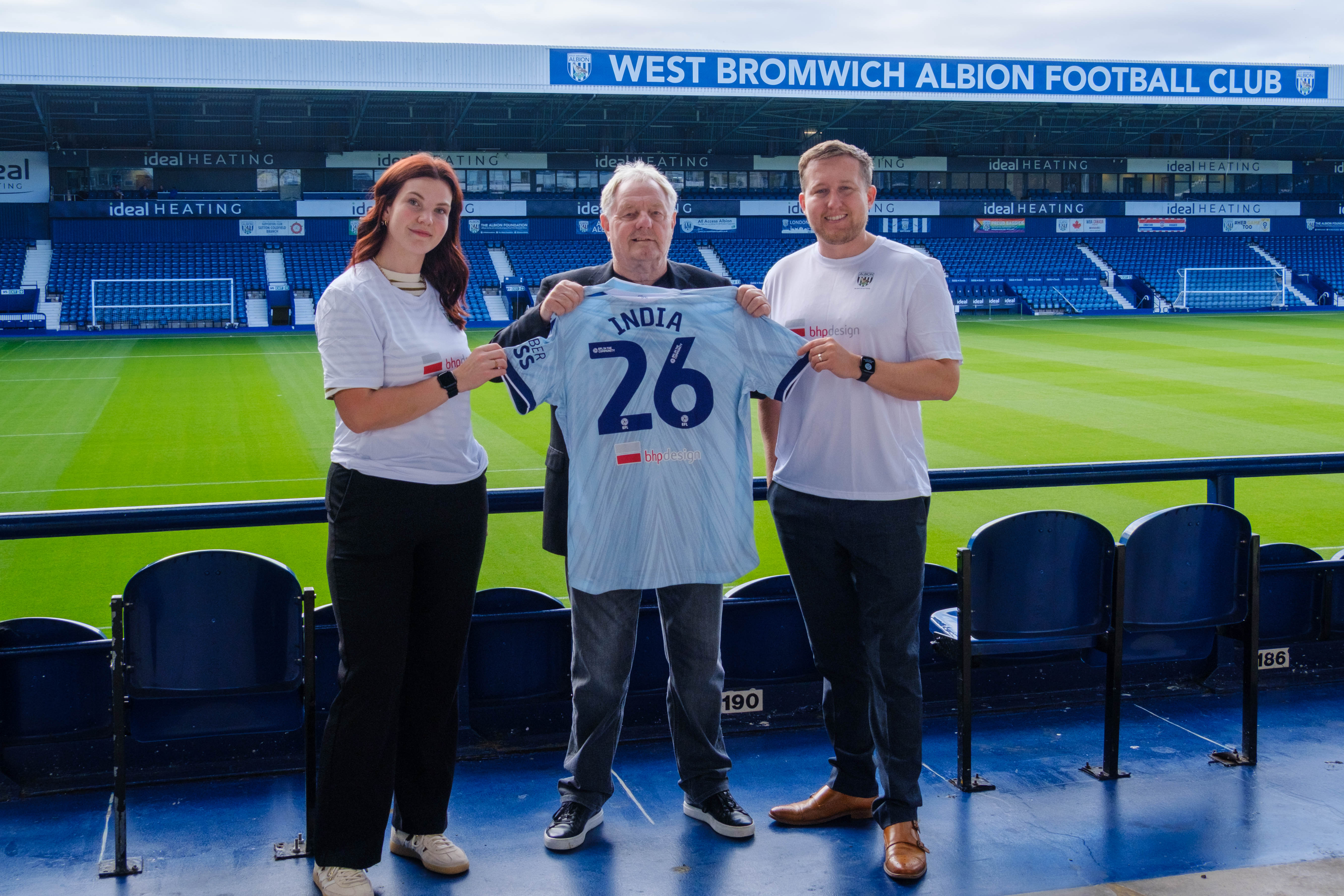 Dave Bloxham, of BHP Design (centre) with Sophie Osbourne (left) and Jonathan Ward, Deputy Director (right) holding a WBA third kit shirt with India 26 on the back.