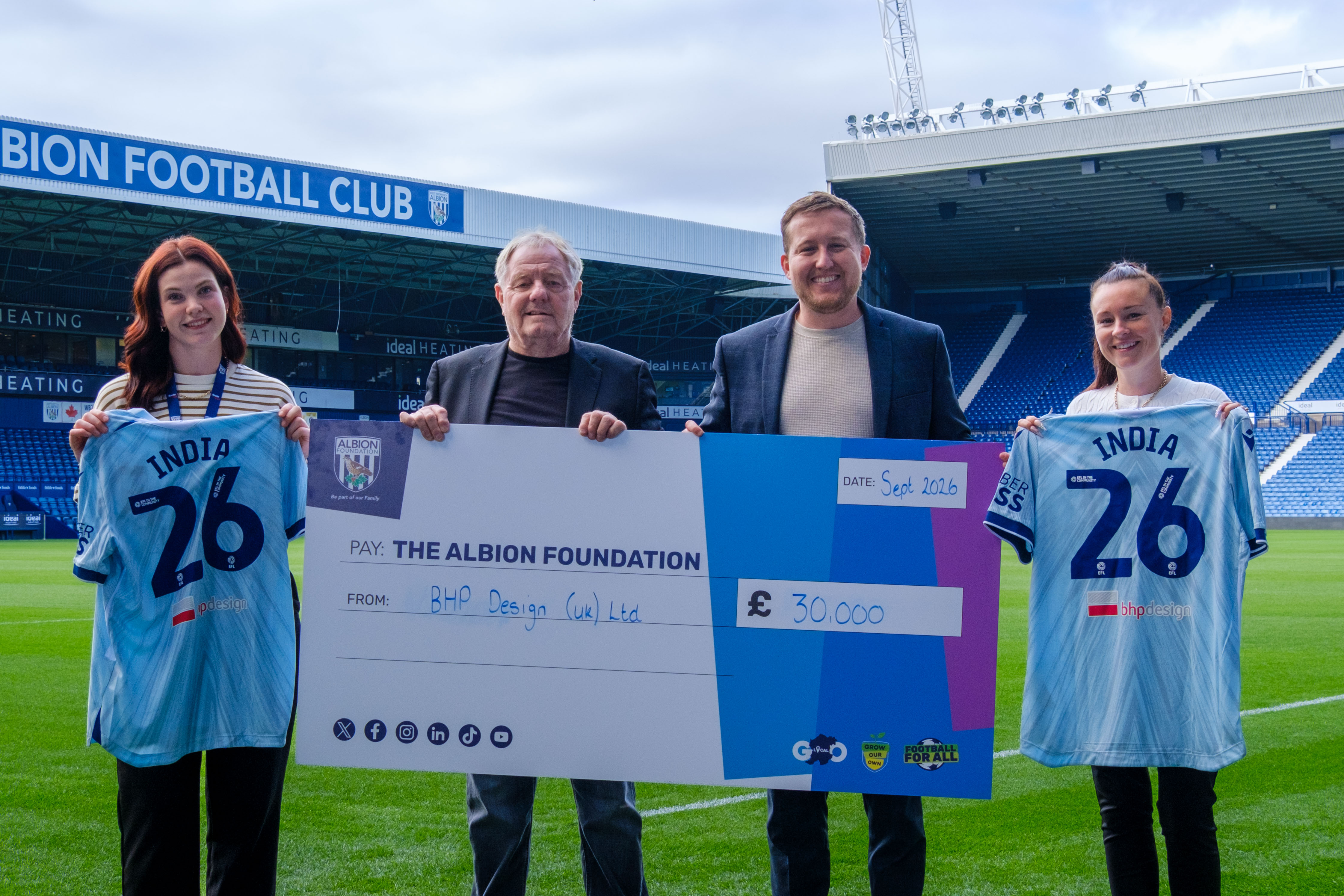 Dave Bloxham, of BHP Design and Jonathan Ward, Deputy Director (centre) holding a large cheque with Sophie Osbourne, Events & Partnerships Coordinator (left) and Jayne Norton, Events & Partnerships Manager (right) holding WBA third kit shirts with India 26 on the back.