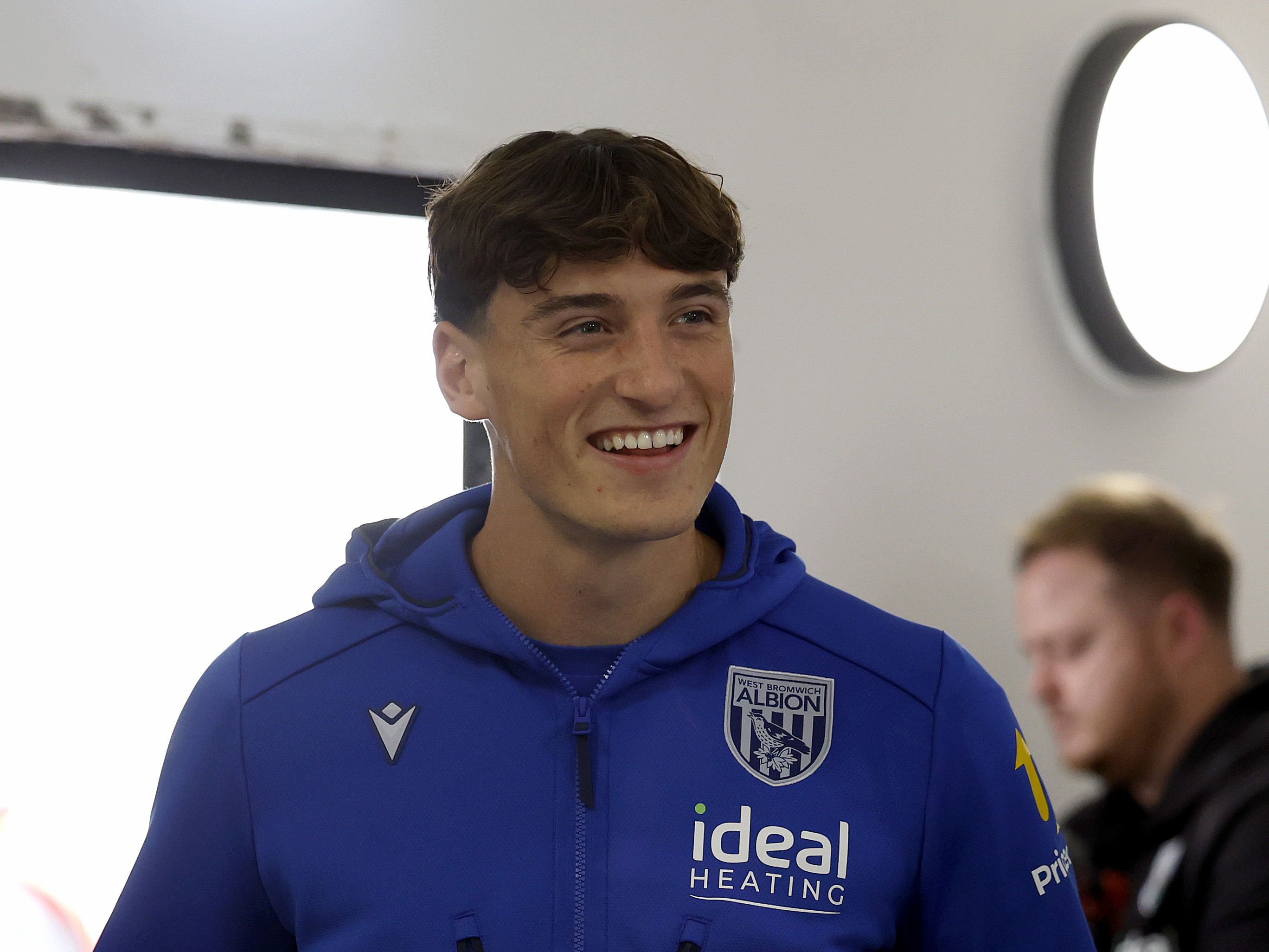 Barney Stewart smiling while arriving for a game in a blue WBA tracksuit 