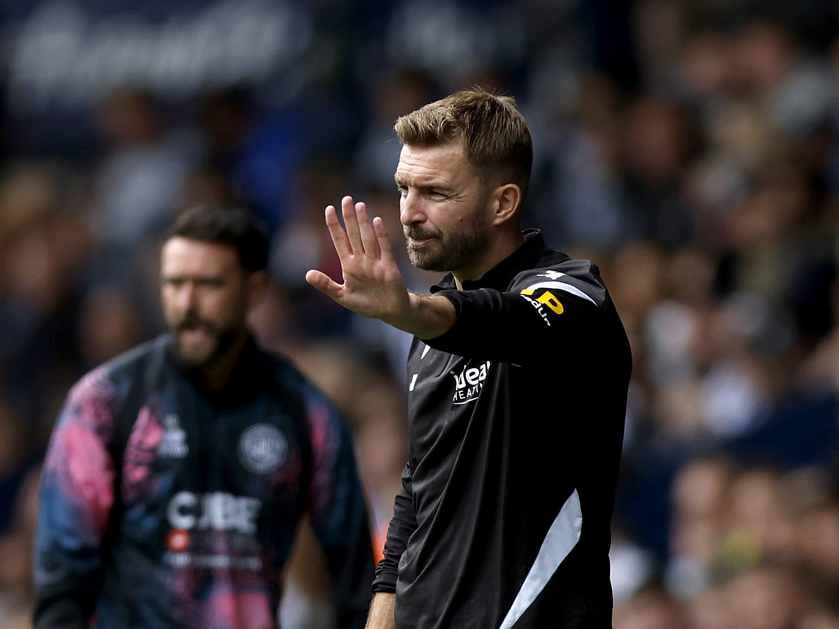 James Morrion holding his hand up on the side of the pitch at The Hawthorns during a game v QPR