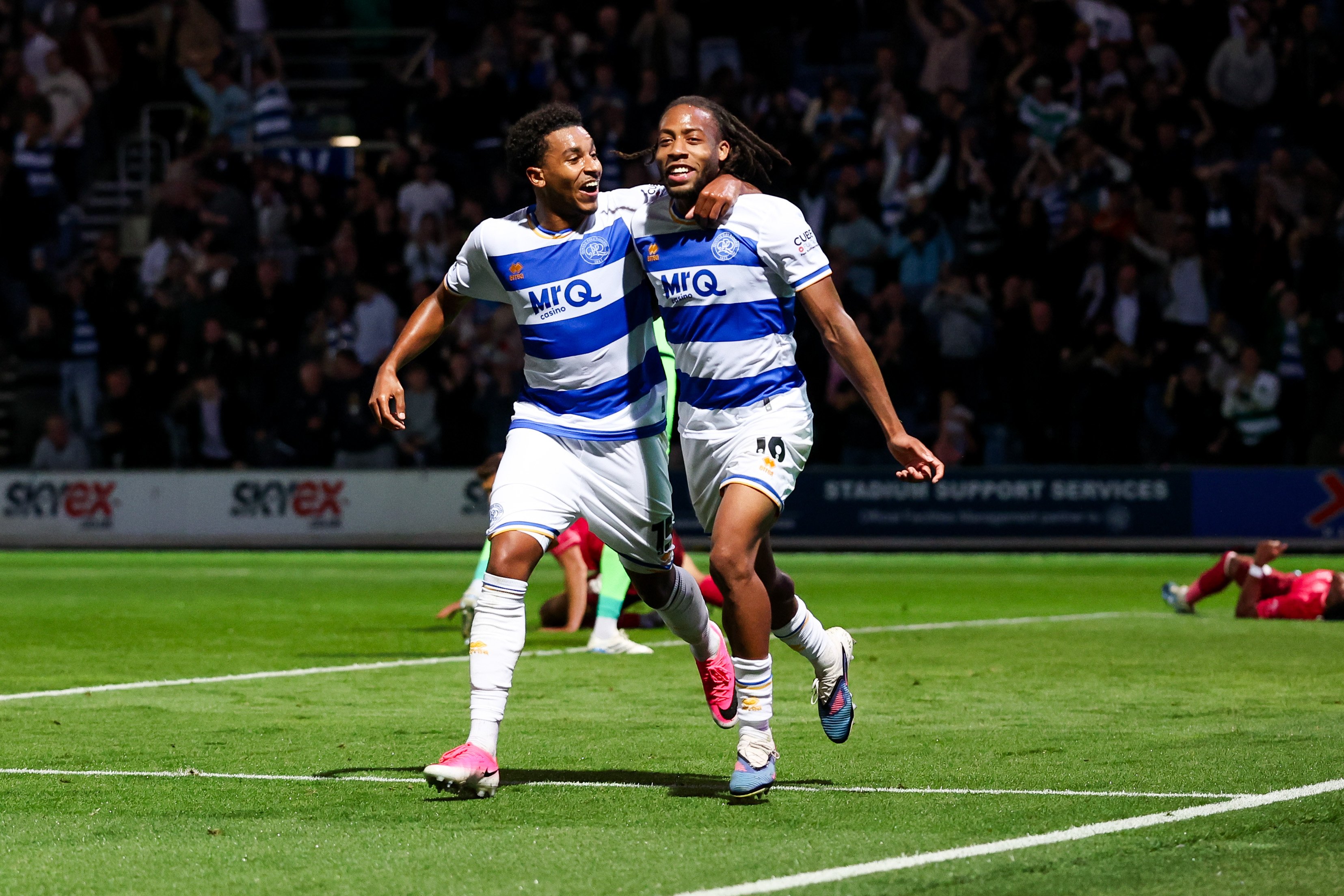 Two QPR players celebrate a goal scored in their home kit 