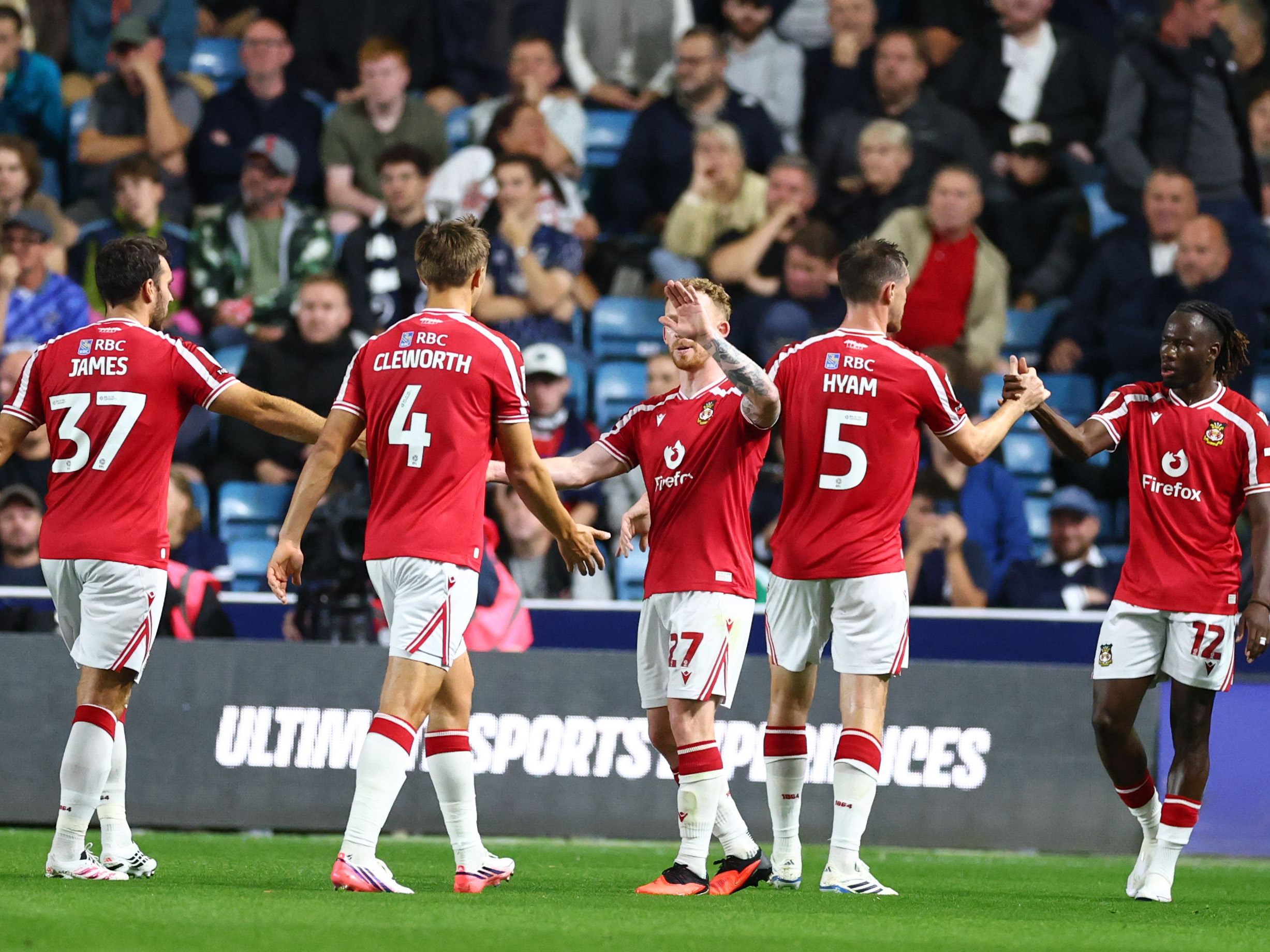 Five Wrexham players in their home kit celebrate a goal scored at Millwall