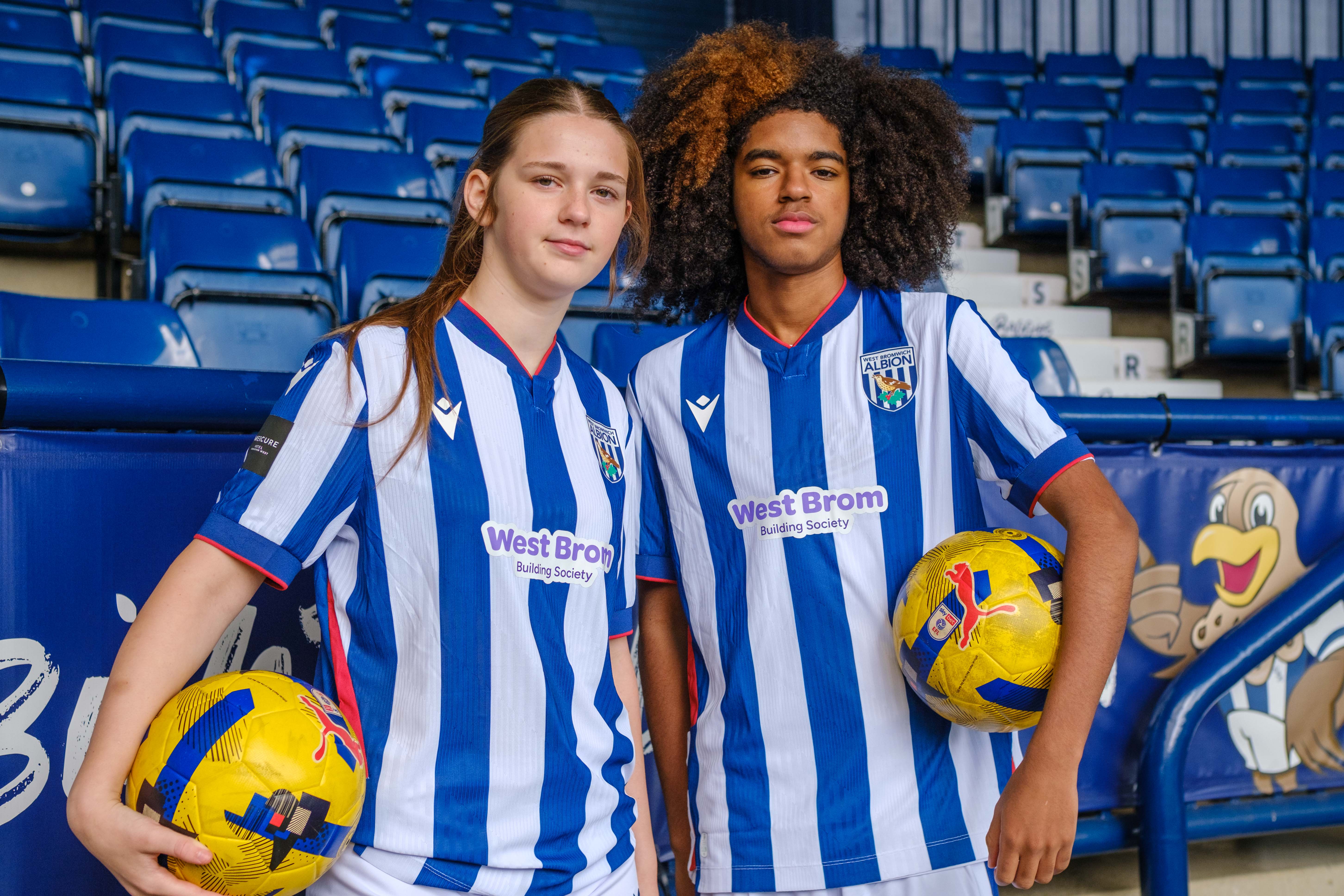 Two Post-16 players standing on the East stand holding a football
