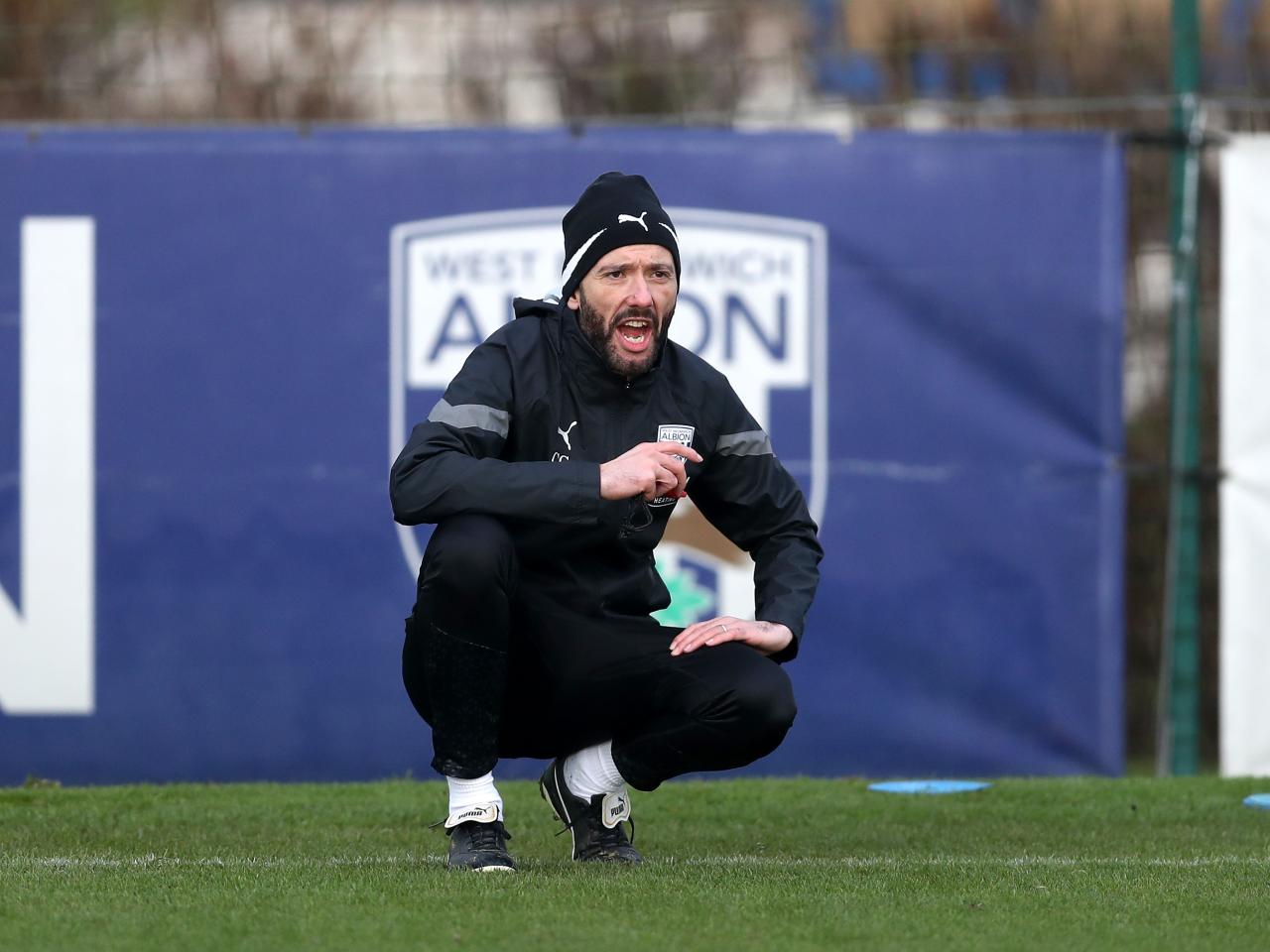 Carlos Corberán crouched down watching training in front of an Albion badge in the background