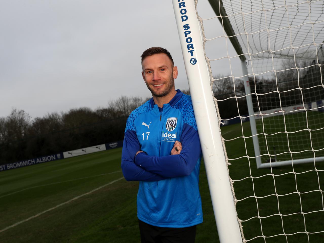 Andi Weimann smiling at the camera while leaning against a goal post