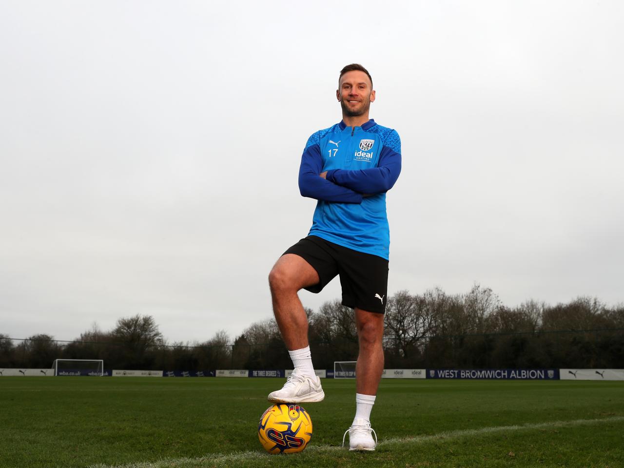 Andi Weimann smiling at the camera stood up with his foot on a ball and his arms folded