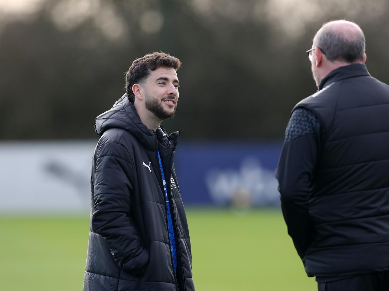 Mikey Johnston watching a training session wearing a big Albion coat and talking to a member of staff