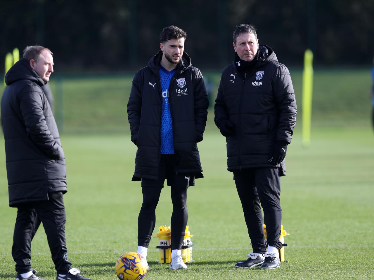 Mikey Johnston watching a training session wearing a big Albion coat and talking to a member of staff
