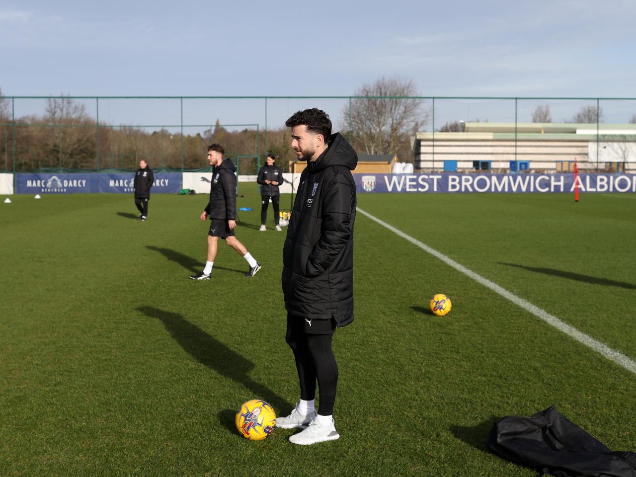 Mikey Johnston watching a training session wearing a big Albion coat