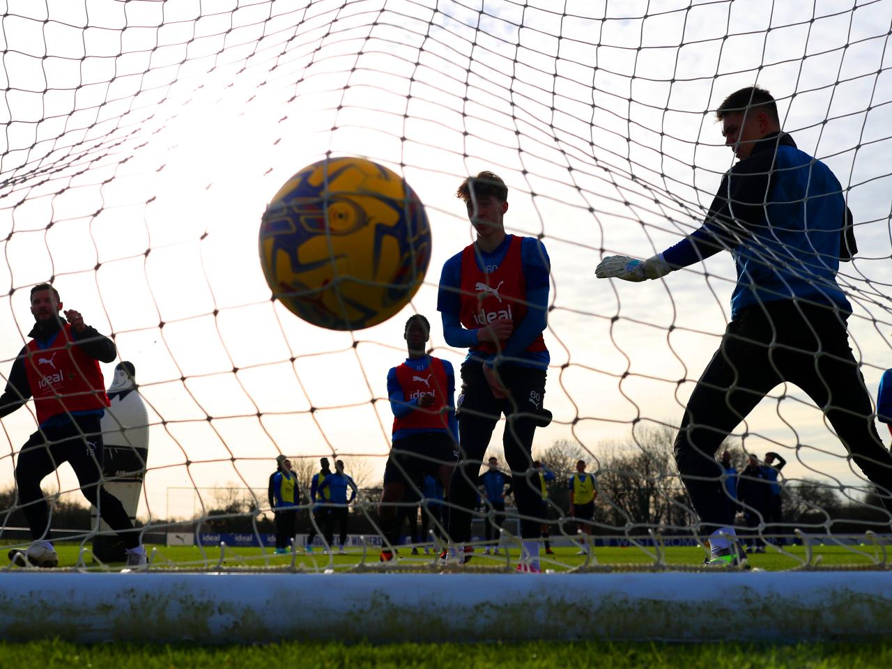A yellow football hitting the back of a goal net during a training session