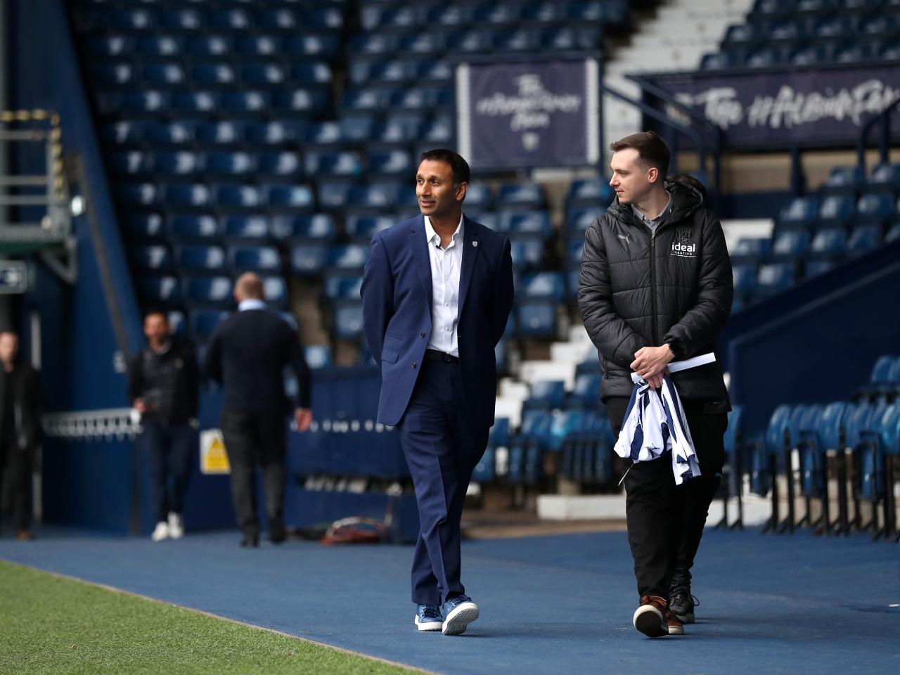 Shilen Patel walking along the blue track in front of the West Stand with West Bromwich Albion's Senior Communications Officer Sean Watts