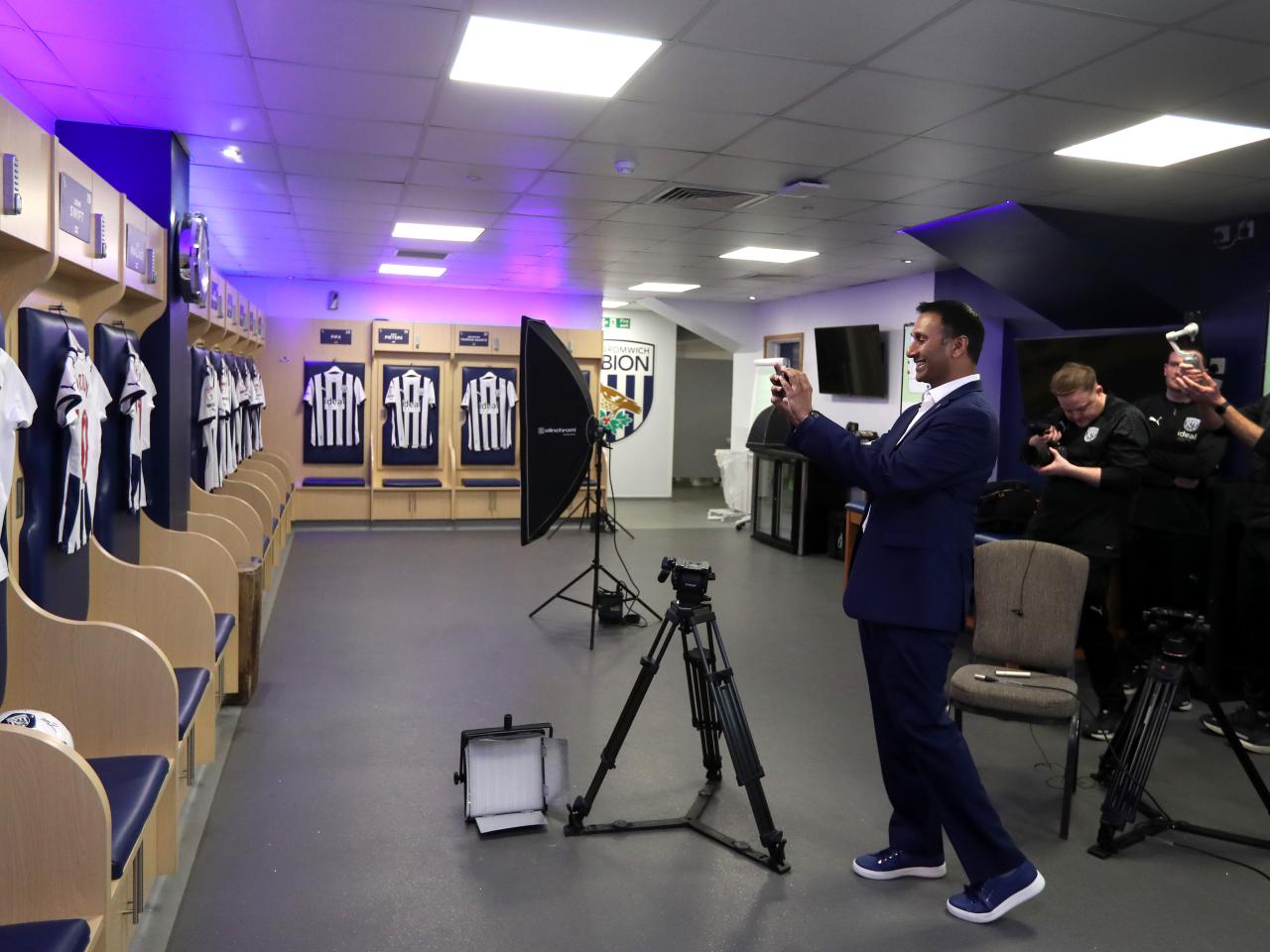 Shilen Patel taking a photo of Albion shirts on his phone in the home dressing room at The Hawthorns