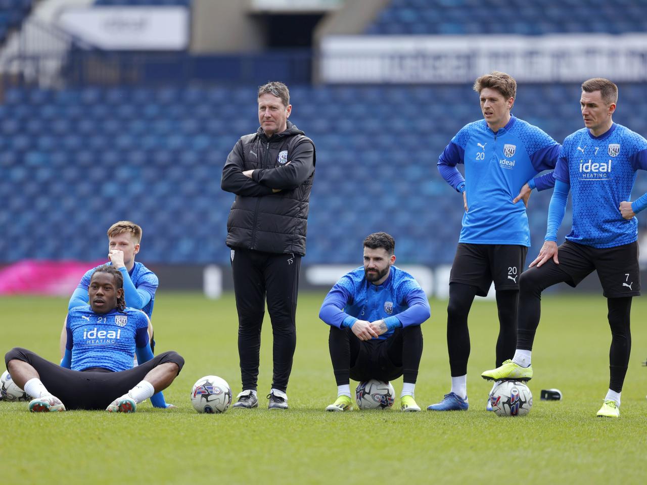 Some Albion players sit on the floor while others stand and watch during a pause in the session at The Hawthorns