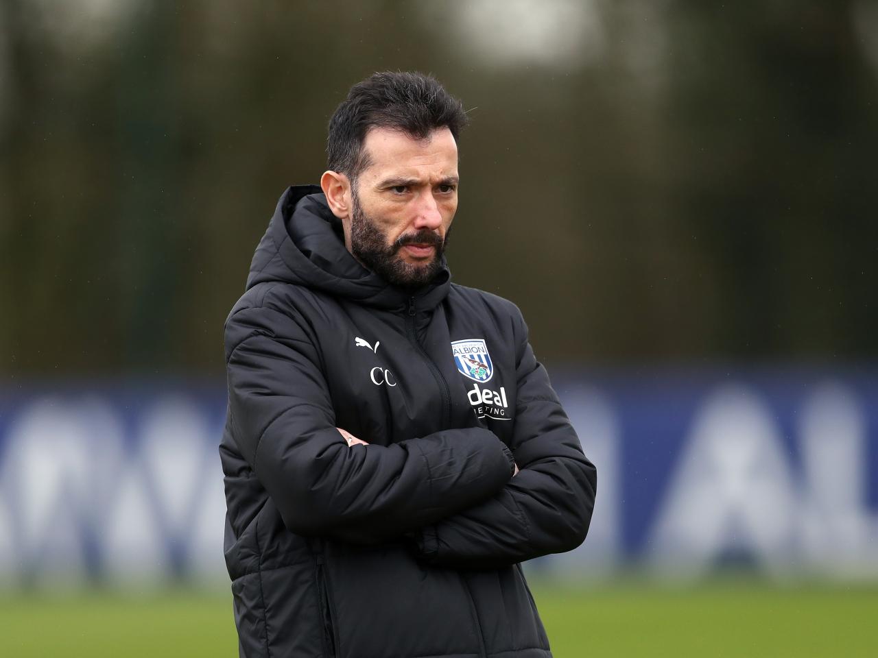 Carlos Corberán wearing a black coat while watching a training session with his arms crossed