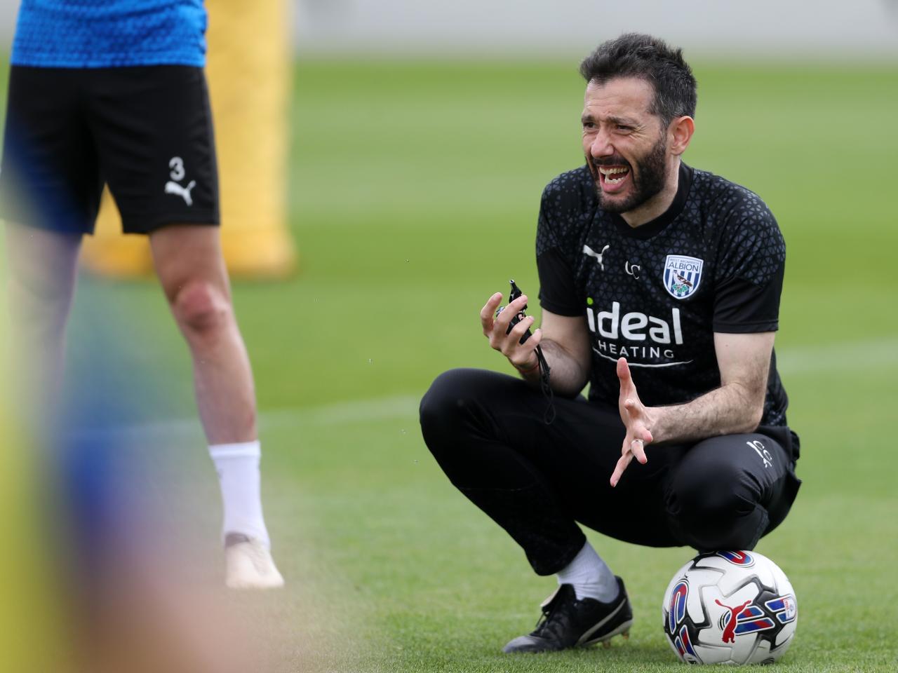 Carlos Corberán crouched down on the training pitch close to a football