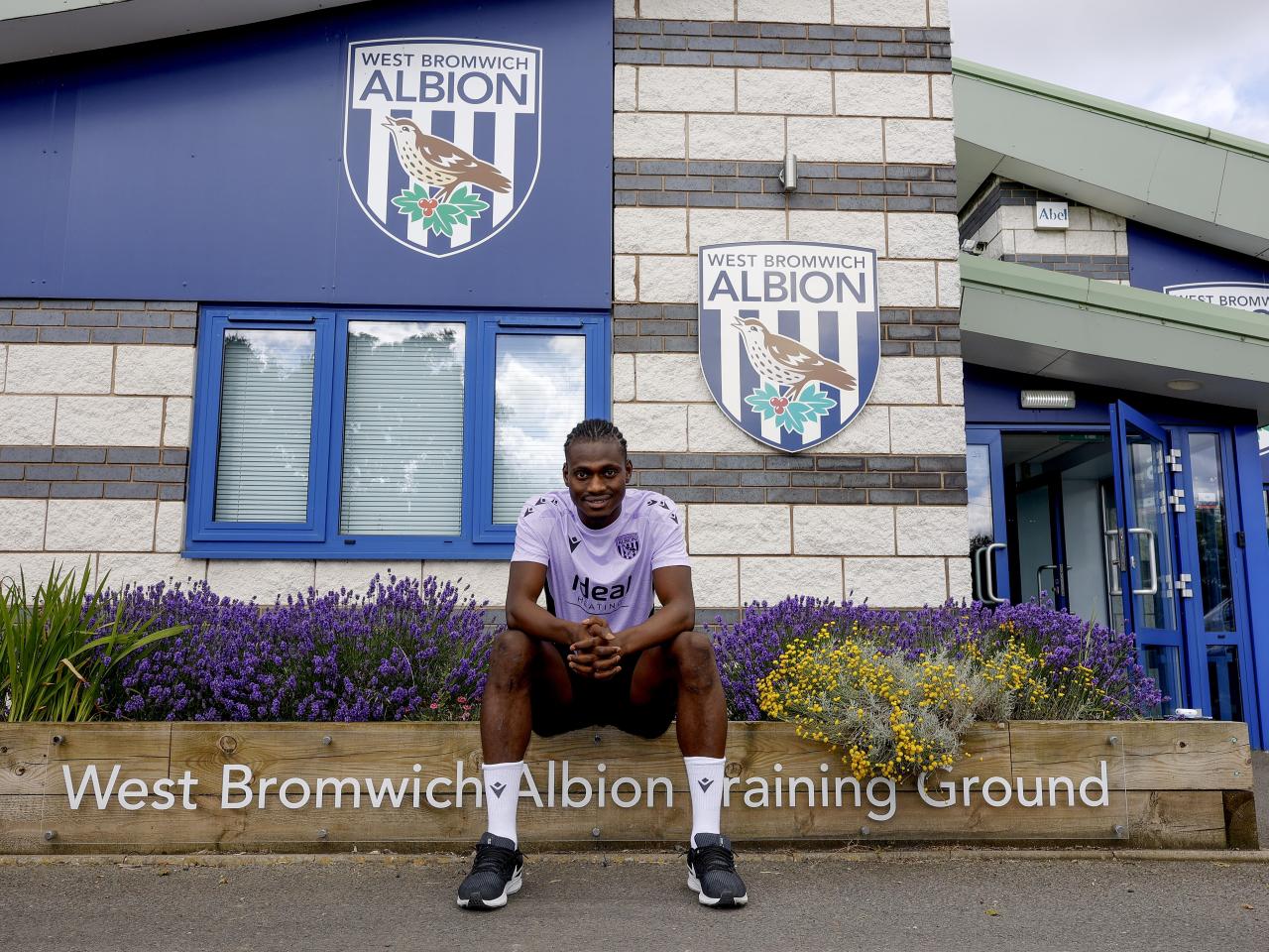 Ousmane Diakité smiling at the camera while sat outside the training ground entrance 