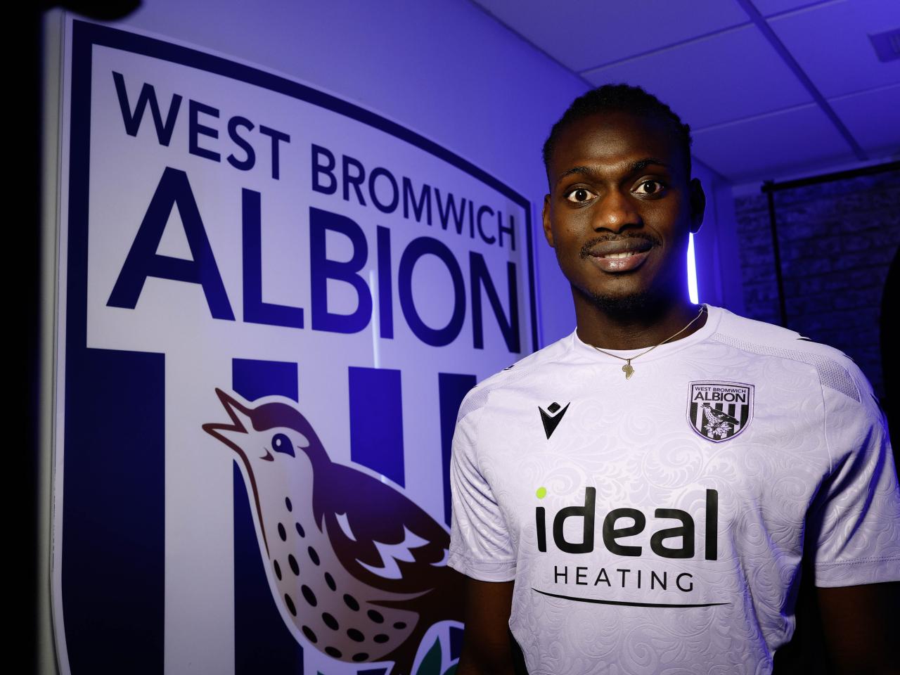Ousmane Diakité smiling at the camera while stood next to a big WBA badge 