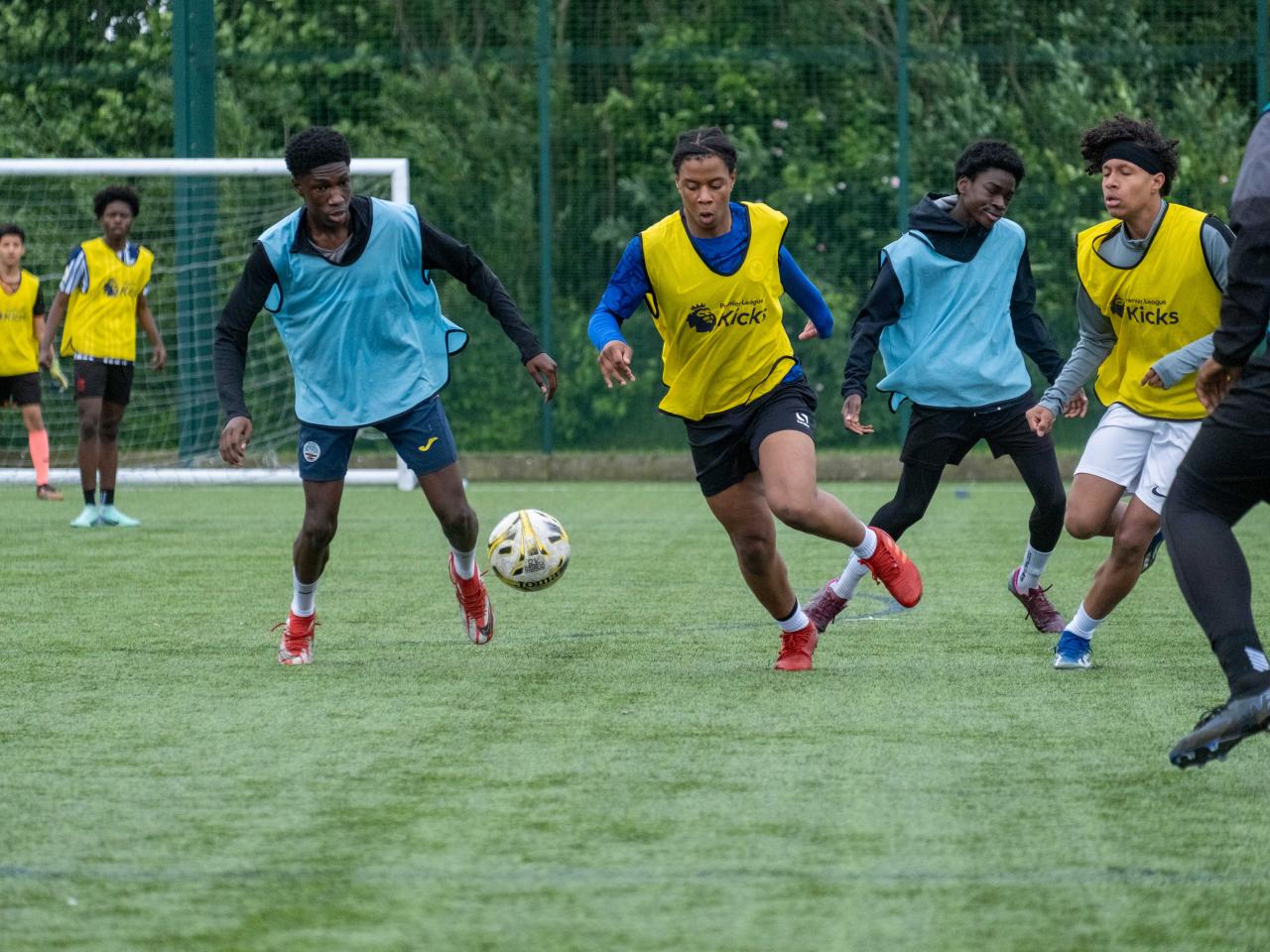 Yellow bibs player chasing the ball, aqua blue players chase.