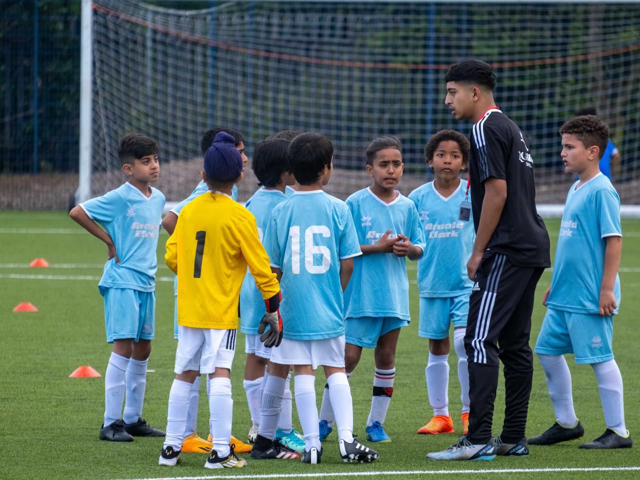 A coach gives instructions to a team wearing sky blue at the South Asian Emerging Talent Festival on the Academy pitch.